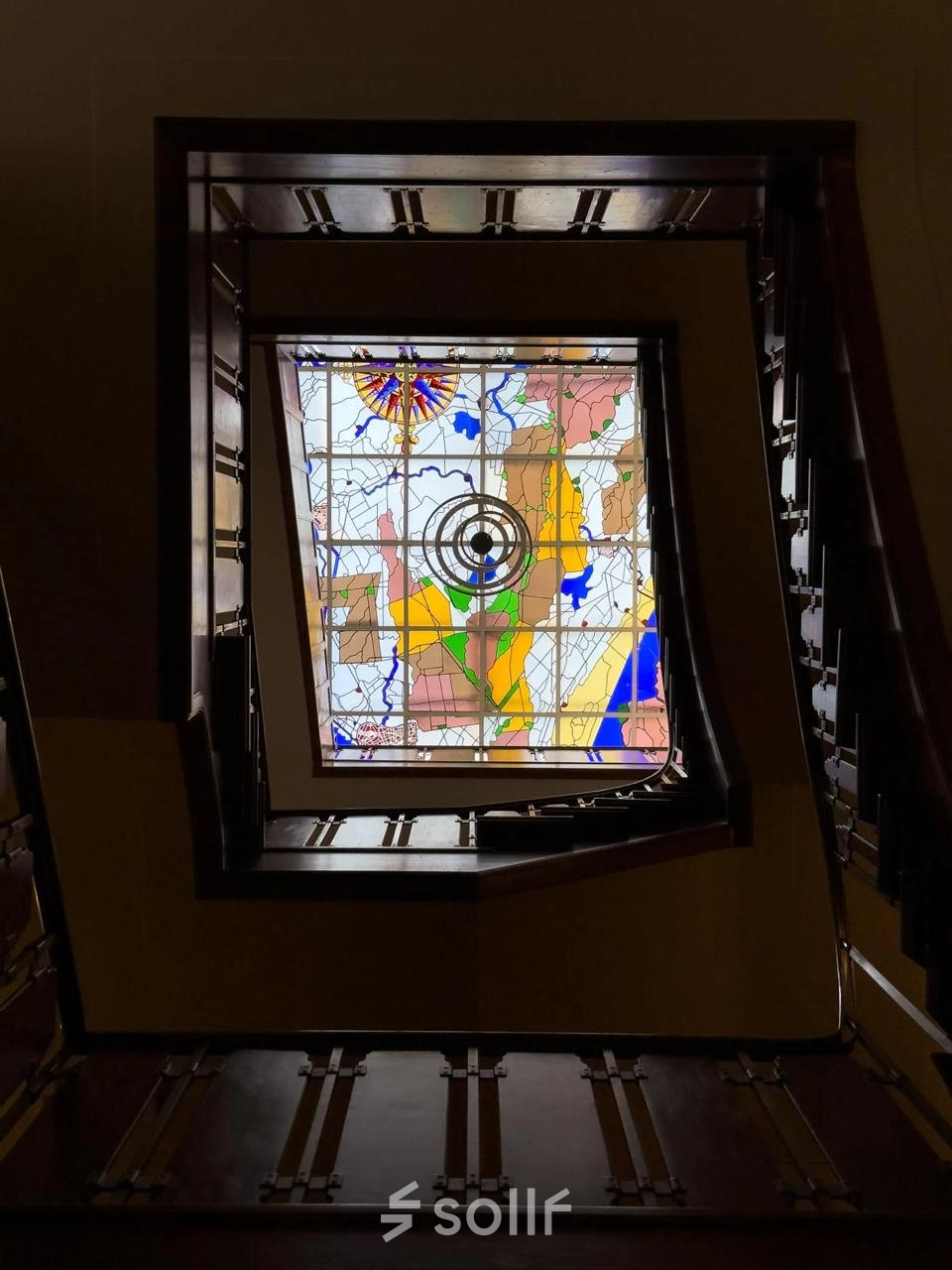 Een kleurrijk glas-in-loodraam met abstracte vormen, gevat in een donkere houten lijst, in een kantoorpand aan Herengracht 582-584, Amsterdam Grachtengordel.