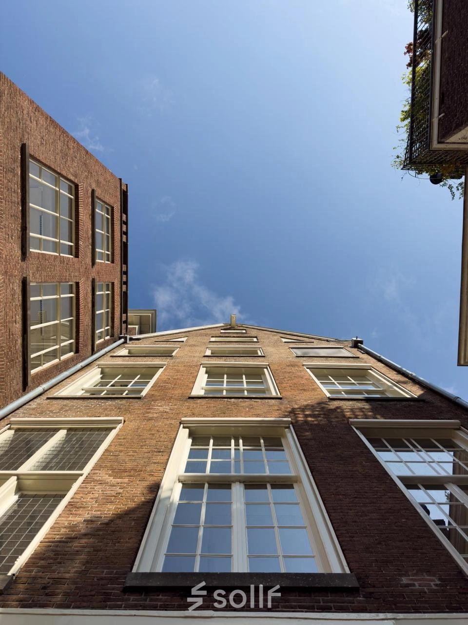 Gevel van een kantoorpand aan de Herengracht 582-584 in Amsterdam met bakstenen en grote ramen onder een heldere lucht.