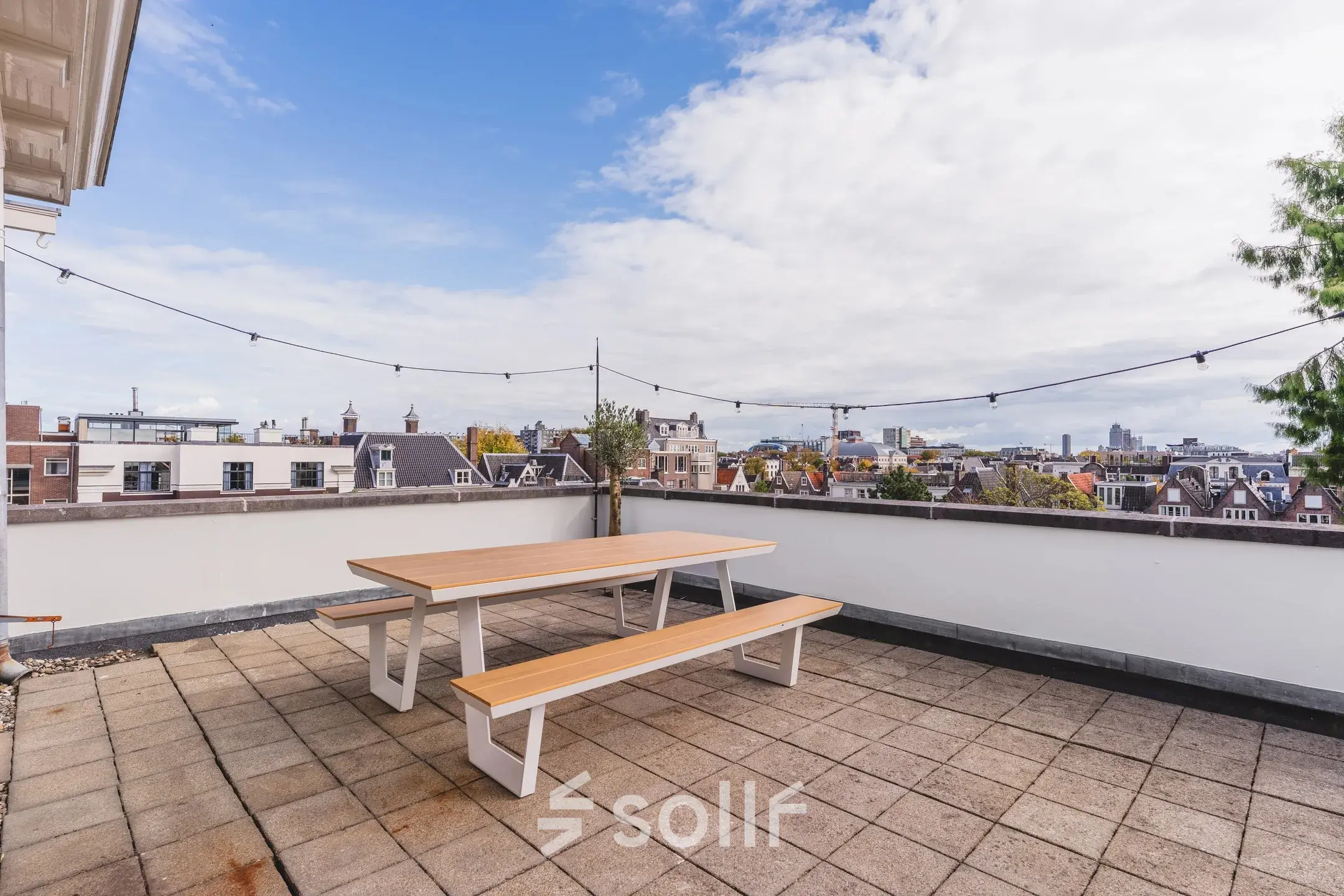 Dakterras in Amsterdam Grachtengordel met houten tafel en banken, uitzicht op de stad. Ideaal voor ontspanning tijdens kantooruren in dit kantoorpand aan de Herengracht 582-584.
