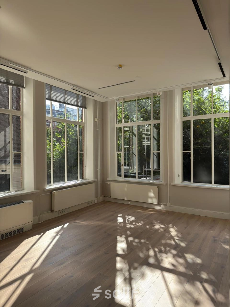 Lichte kantoorruimte te huur met grote ramen aan de Herengracht 582-584, Amsterdam Grachtengordel, zonder meubilair, met uitzicht op de binnentuin en houten vloeren.