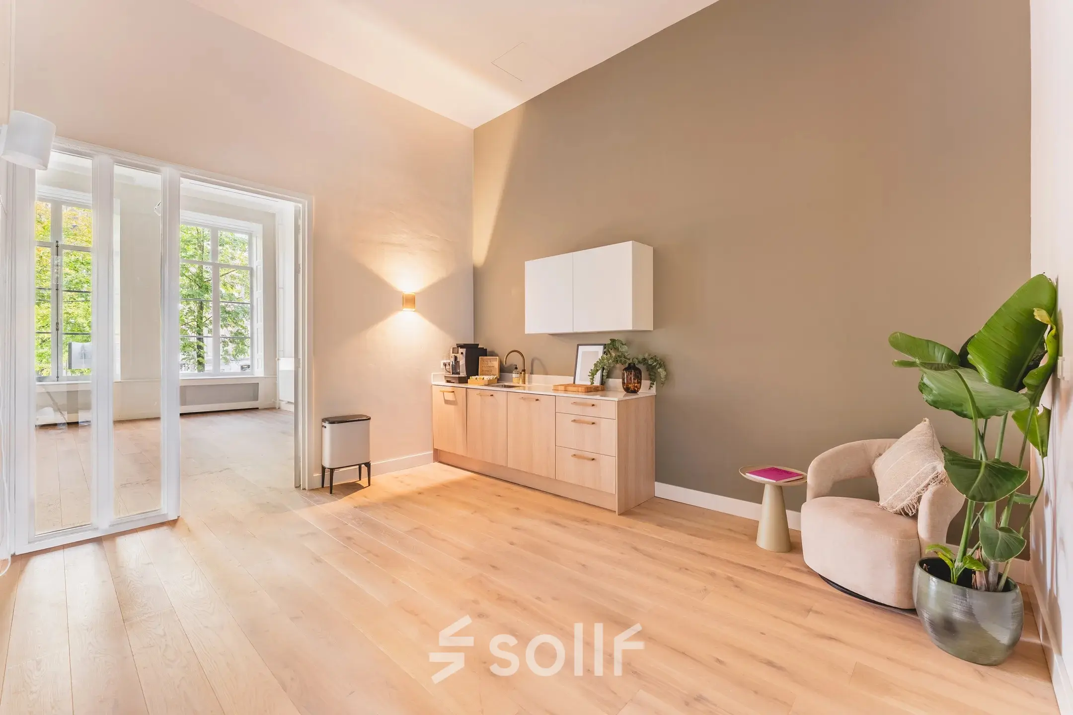 Een lichte en uitnodigende kantoorruimte met houten vloer, een kitchenette, en comfortabele zitgelegenheid aan de Herengracht in Amsterdam, ideaal om te huren als kantoorpand.