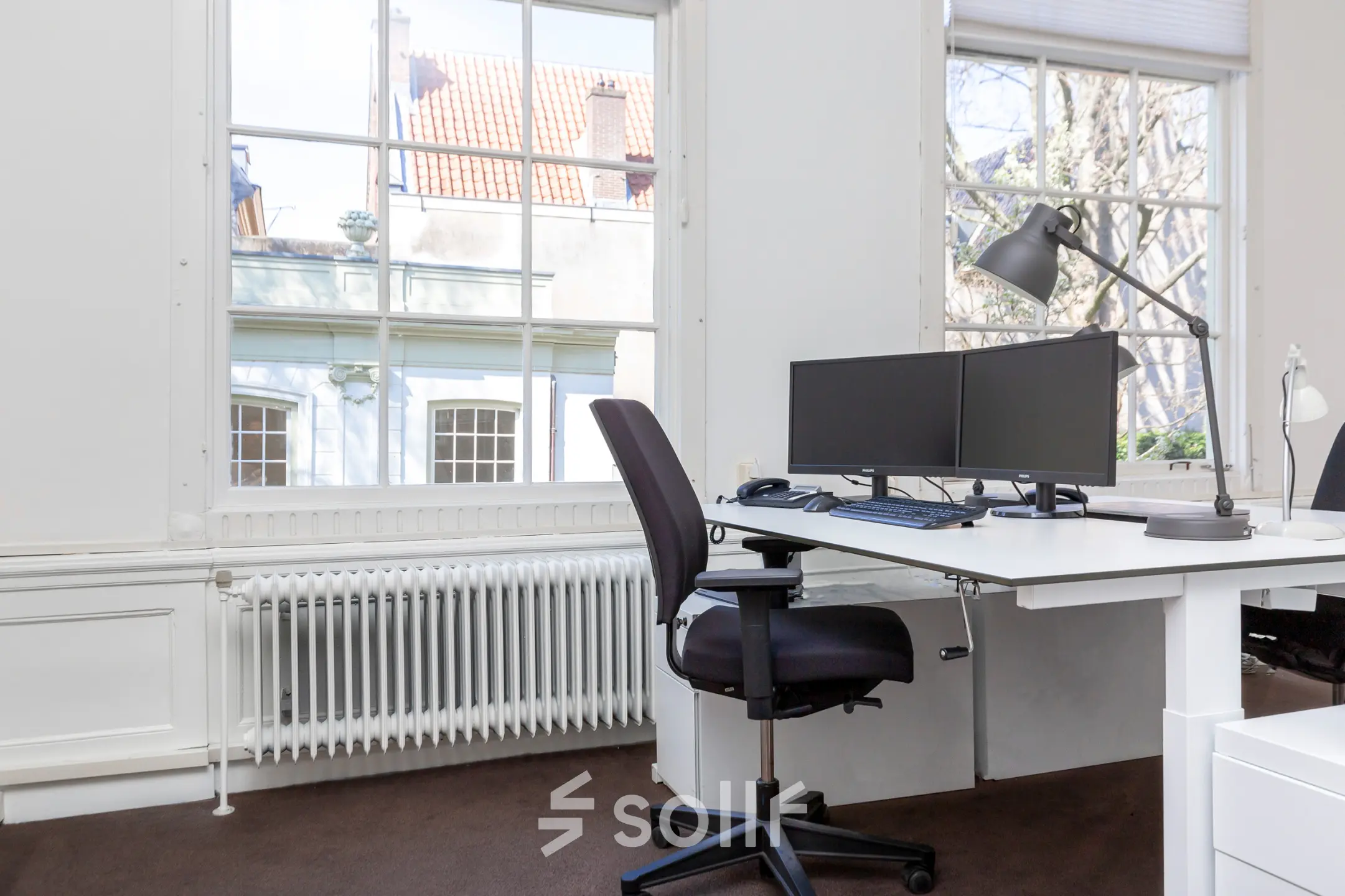 Lichte kantoorruimte met bureau, stoel en twee computerschermen, gelegen aan de Keizersgracht 62-64 in de Amsterdam Grachtengordel.