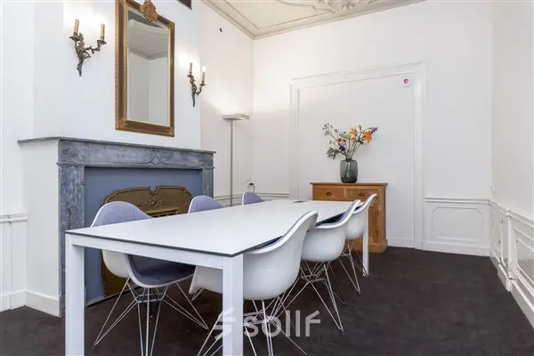 Stijlvolle kantoorruimte met een lange witte tafel en moderne stoelen op Keizersgracht 62-64, Amsterdam Grachtengordel. Een klassieke open haard en decoratieve elementen geven de ruimte karakter.