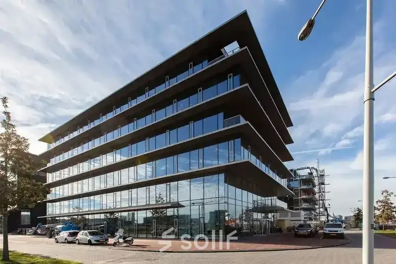 Modern kantoorpand op de Moermanskkade 303 in Amsterdam Houthavens, ideaal voor kantoorruimte huren. Het glazen gebouw weerspiegelt de lucht, met enkele auto's voor het pand geparkeerd.