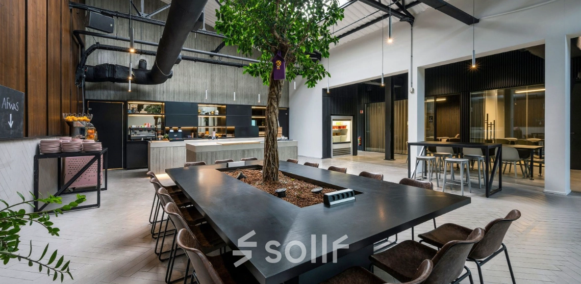 Kantoorruimte huren aan Meeuwenlaan 98-100 in Amsterdam Noord, met een grote tafel omringd door stoelen en een centrale boom, geschikt voor samenwerkingssessies.