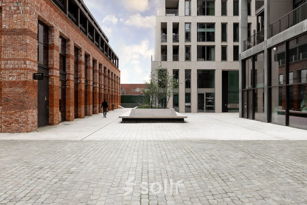 Buitenaanzicht van een modern kantoorpand op Papaverhof 58 in Amsterdam Noord, met elegante bakstenen en glasconstructie. Een enkele persoon loopt over het plein voor het gebouw.