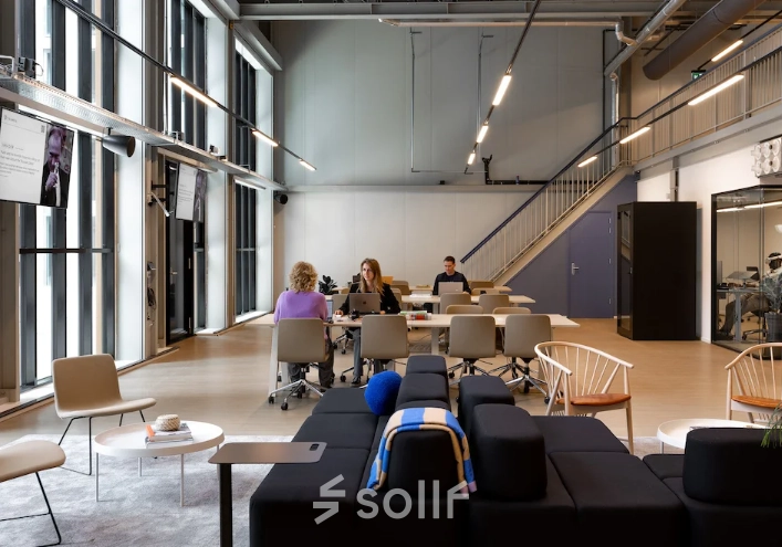 Kantoorruimte huren aan Papaverhof 58, Amsterdam Noord met moderne werkplekken en grote ramen. Verschillende mensen zijn bezig met zakelijke activiteiten aan tafels.