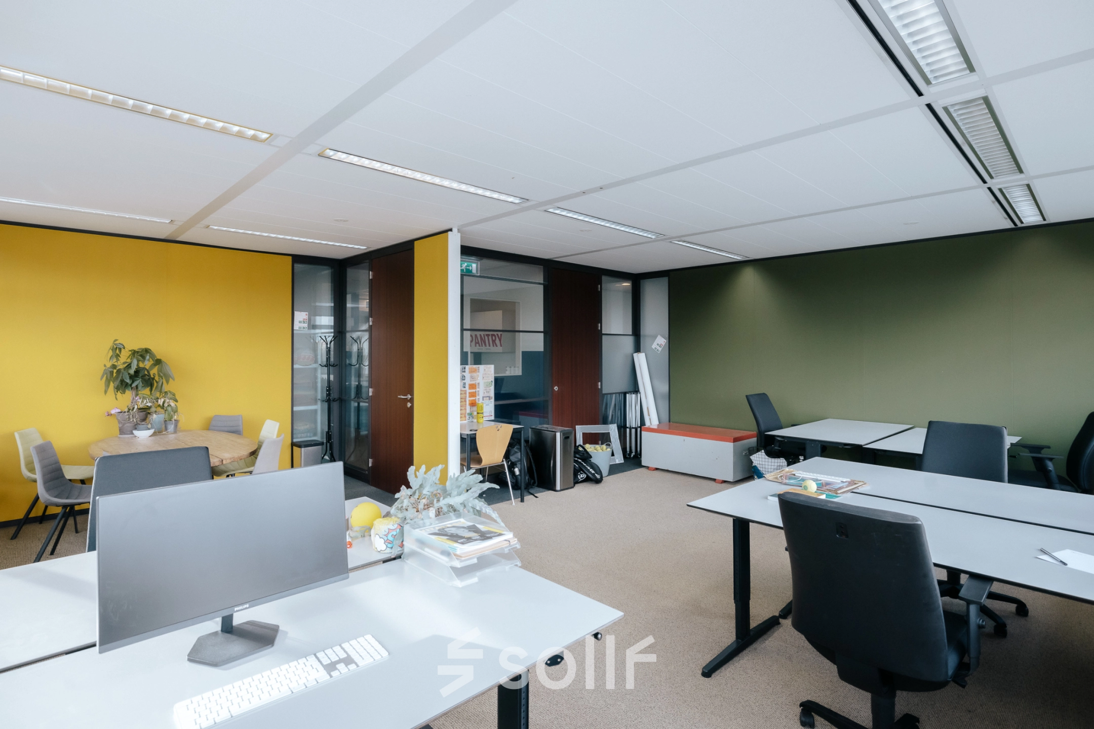 Kantoorruimte in Amsterdam Noord op TT Vasumweg 44 met bureaus, computers en een gele muur.