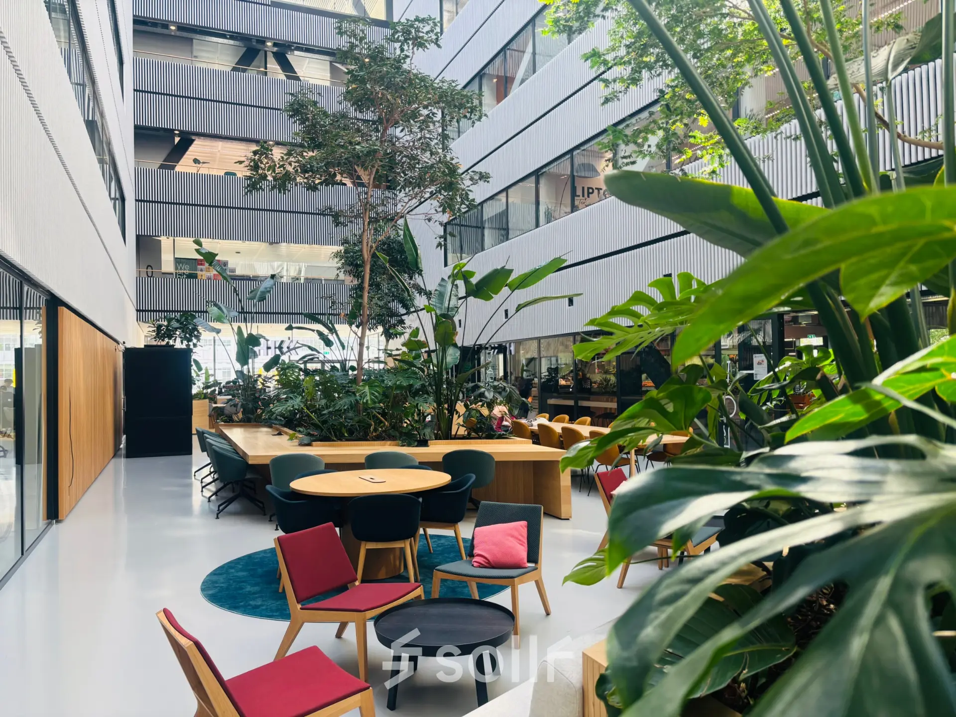 Ruim atrium met veel groen en kleurrijk meubilair in kantoorpand op Science Park 301, Amsterdam Oost. Ideaal voor kantoorruimte huren met een open en uitnodigende sfeer.