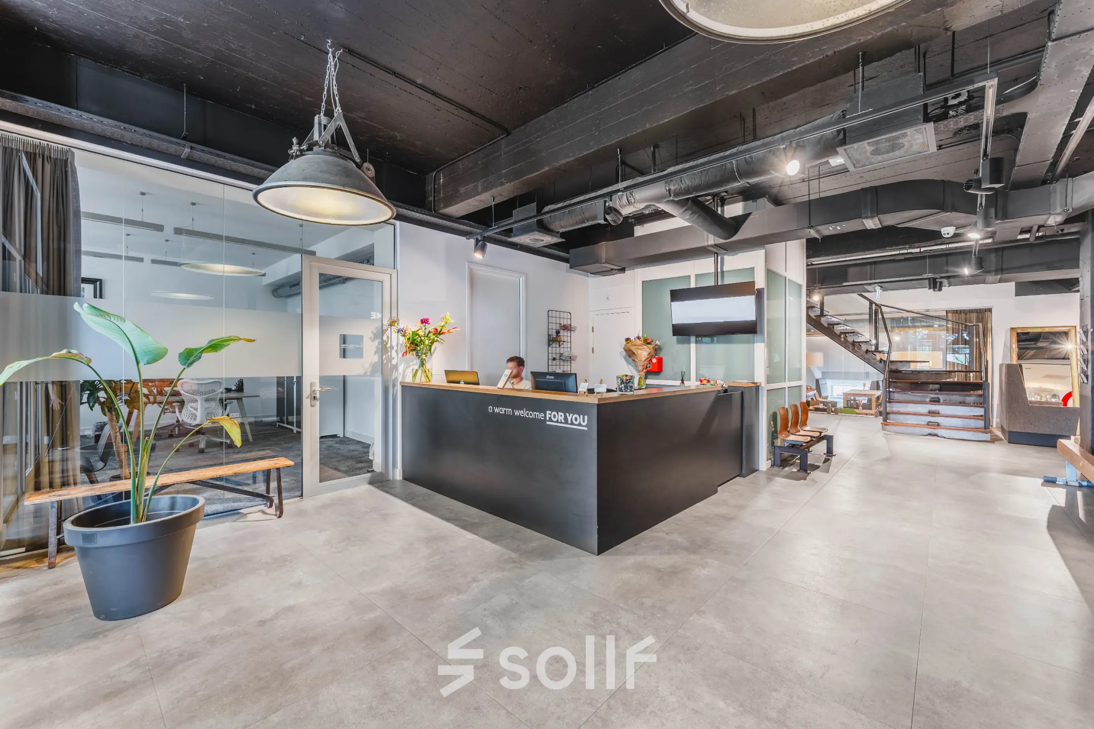 Moderne receptie met balie en ontvangstgedeelte in een kantoorpand op Olympisch Stadion 24-28, Amsterdam Oud Zuid. Een vrouw zit achter de balie en verwelkomt bezoekers.