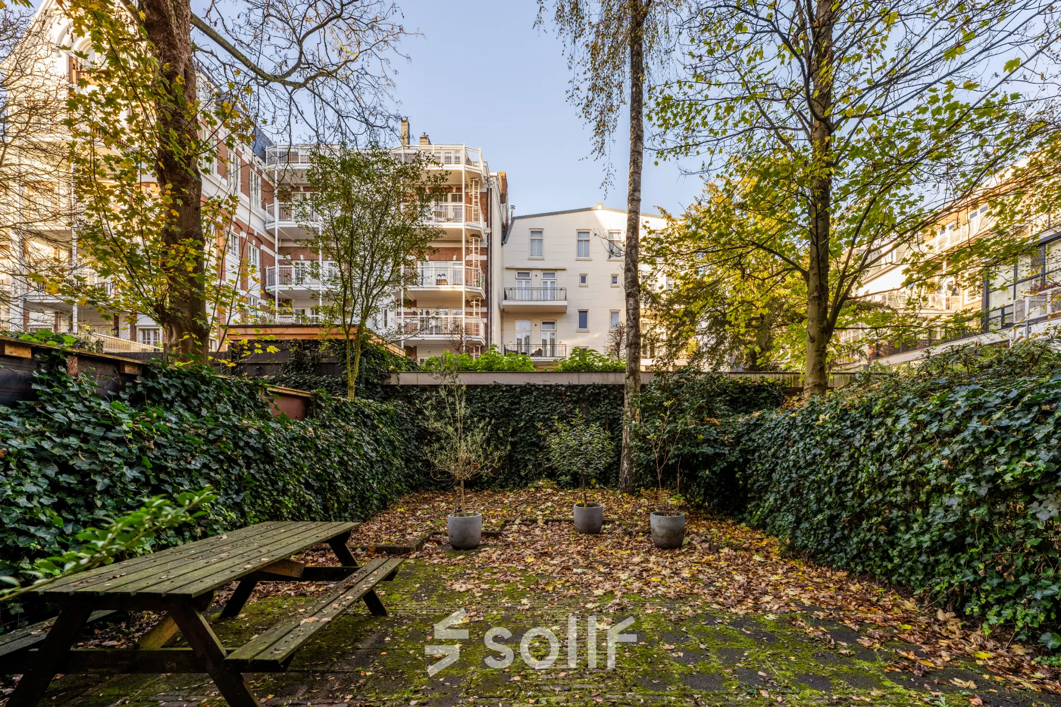 Buitenzicht op een groene patio omgeven door hoge woongebouwen op PC Hooftstraat 150, Amsterdam Oud Zuid, ideaal voor ontspanning in kantoorpand. Huur deze kantoorruimte voor een inspirerende werkomgeving.