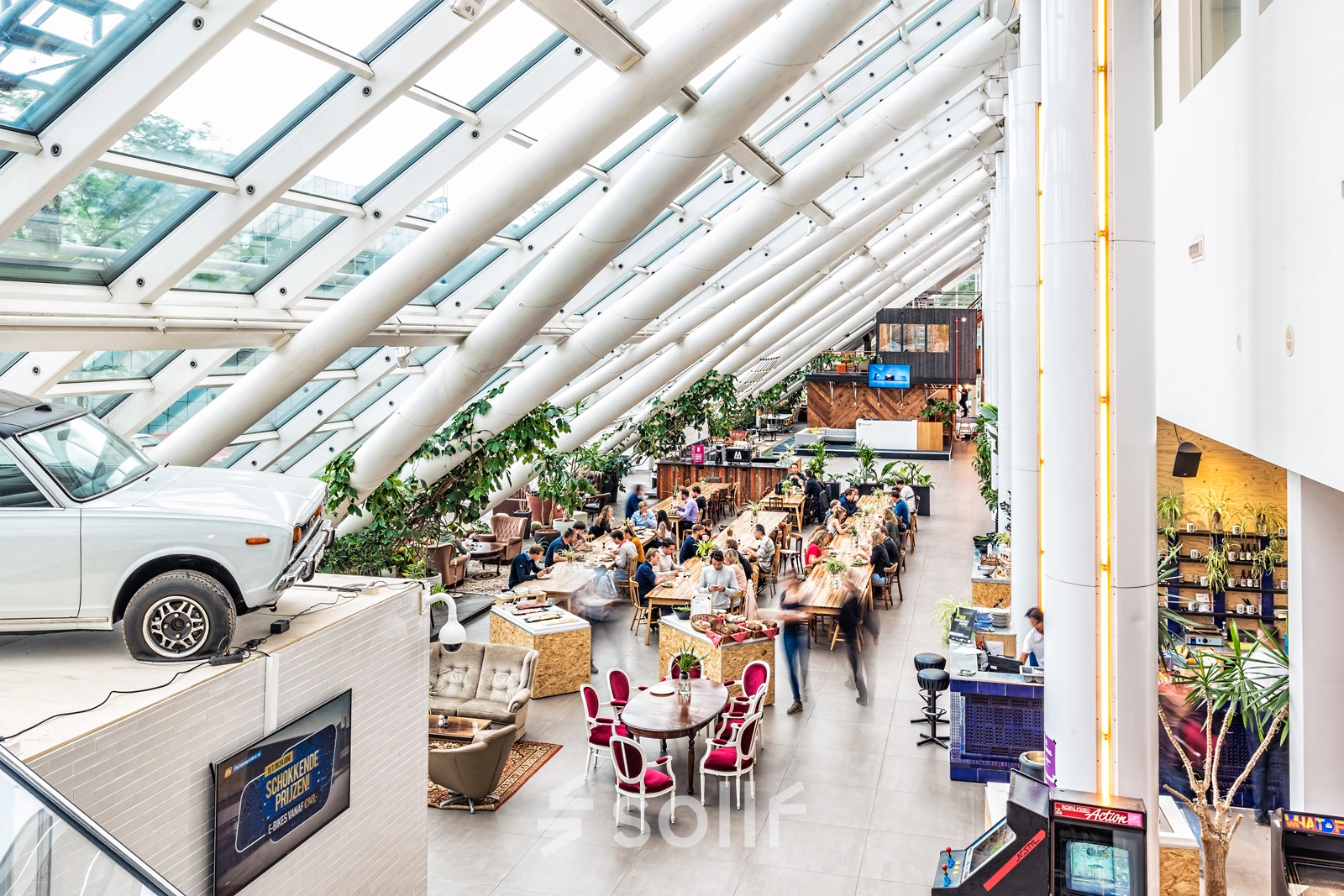 Ruime en lichte kantoor met glazen dak op Johan Huizingalaan 400, Amsterdam Riekerpolder, vol met mensen die samenwerken aan tafels.