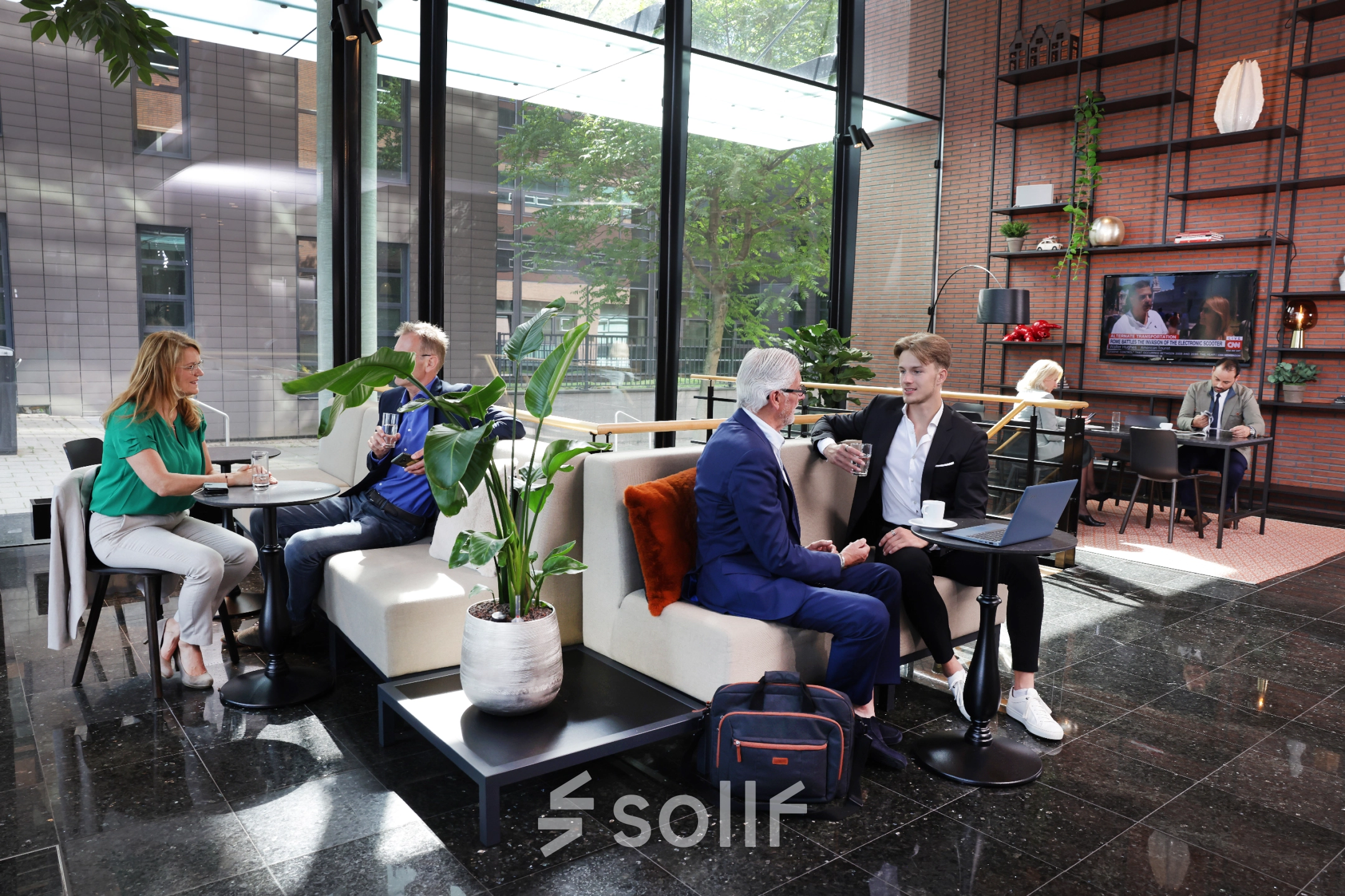 Moderne kantoorruimte aan de Teleportboulevard 110 in Amsterdam Sloterdijk met mensen die vergaderen en koffie drinken tussen planten en stijlvol meubilair.