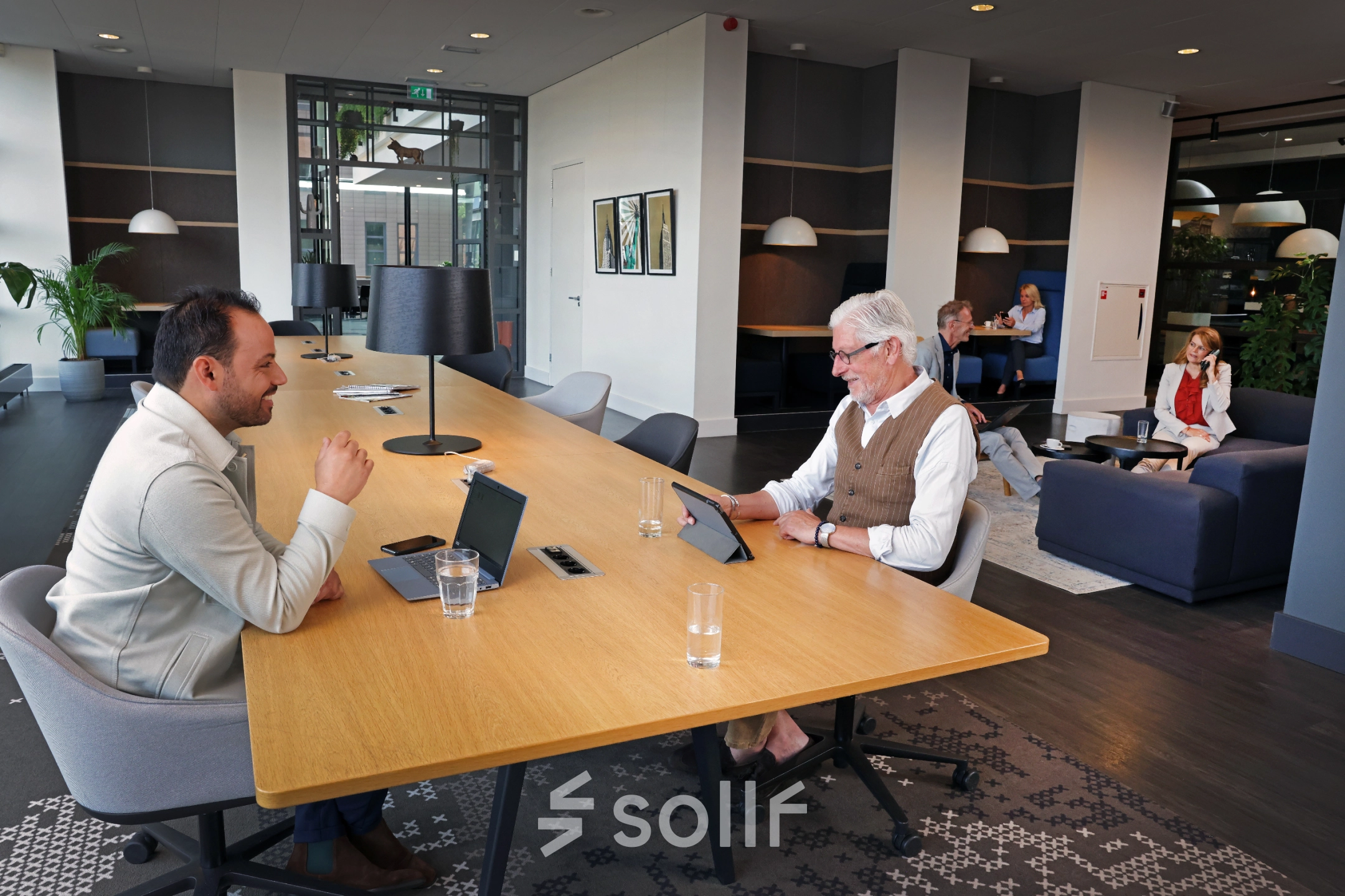 Zakelijke mensen werken in een moderne kantoorruimte met lange houten tafel en comfortabele stoelen in Amsterdam Sloterdijk aan de Teleportboulevard 110.
