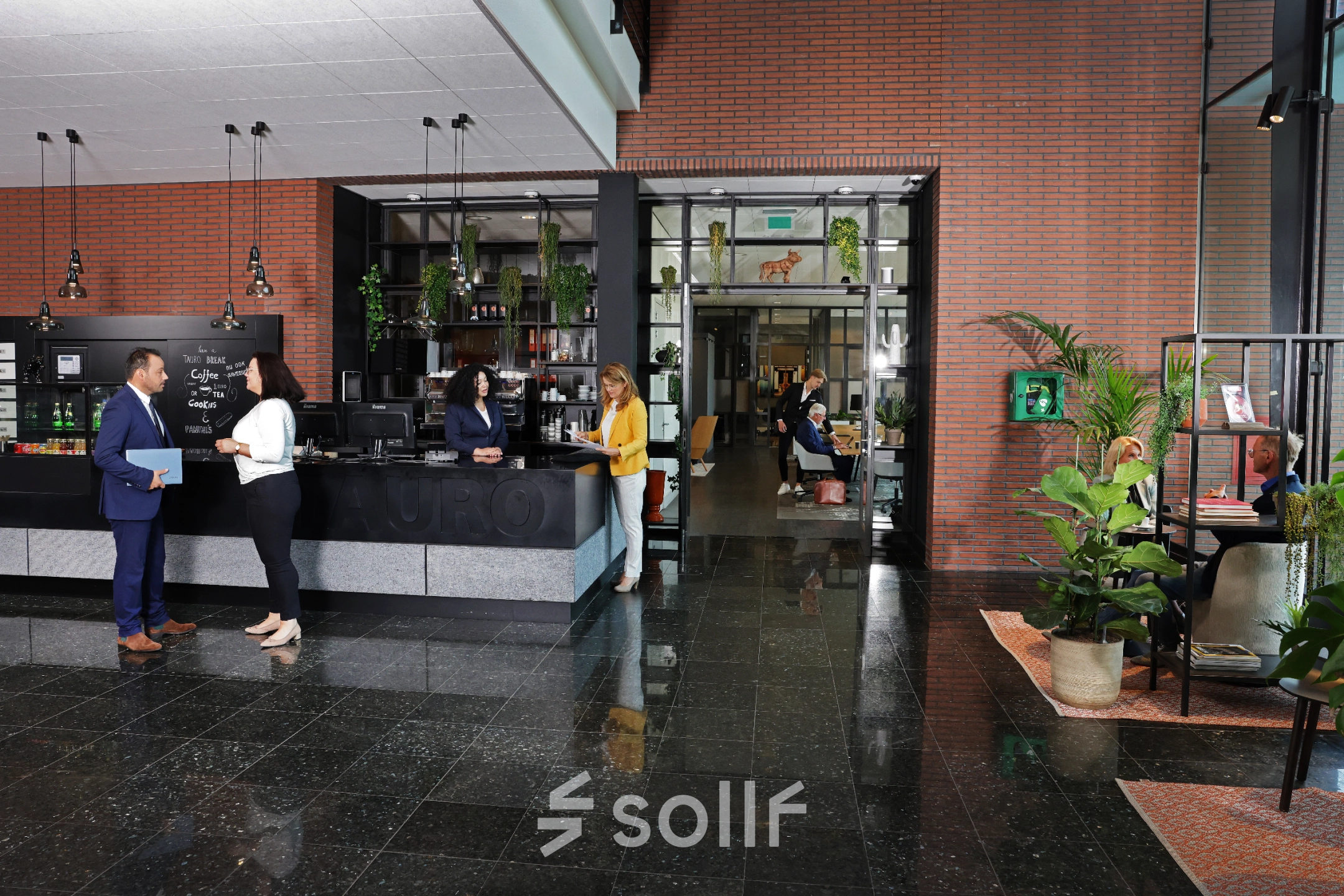 Moderne kantoorruimte aan Teleportboulevard 110 in Amsterdam Sloterdijk met een stijlvolle receptie. Mensen voeren zakelijke gesprekken aan de balie en werken in een aangrenzende ruimte. Planten en decoratie zorgen voor een gastvrije sfeer.