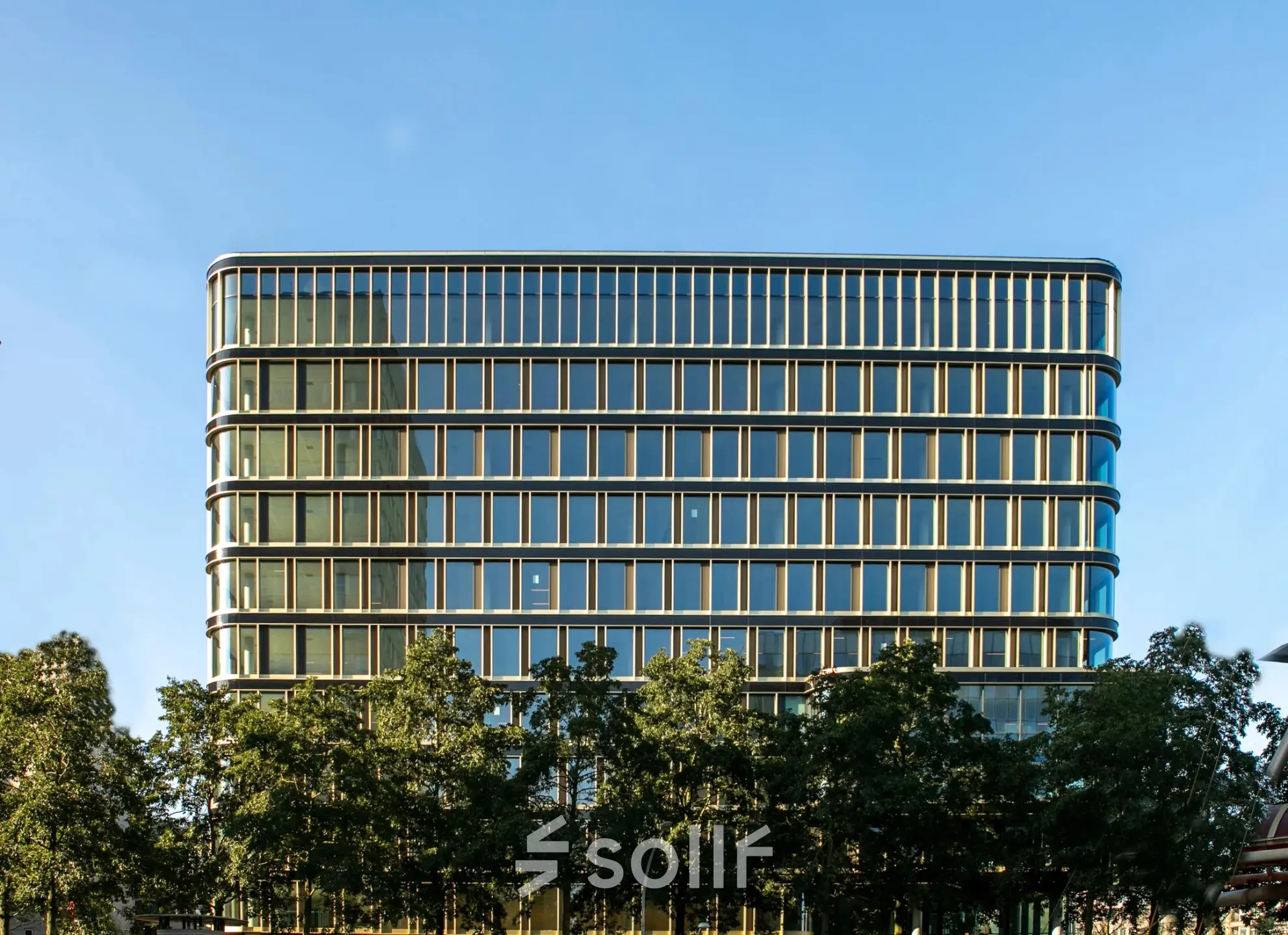 Modern kantoorpand aan het Kon. Wilhelminaplein 4 in Amsterdam West met glazen gevel en omliggende bomen, ideaal voor kantoorruimte huren.