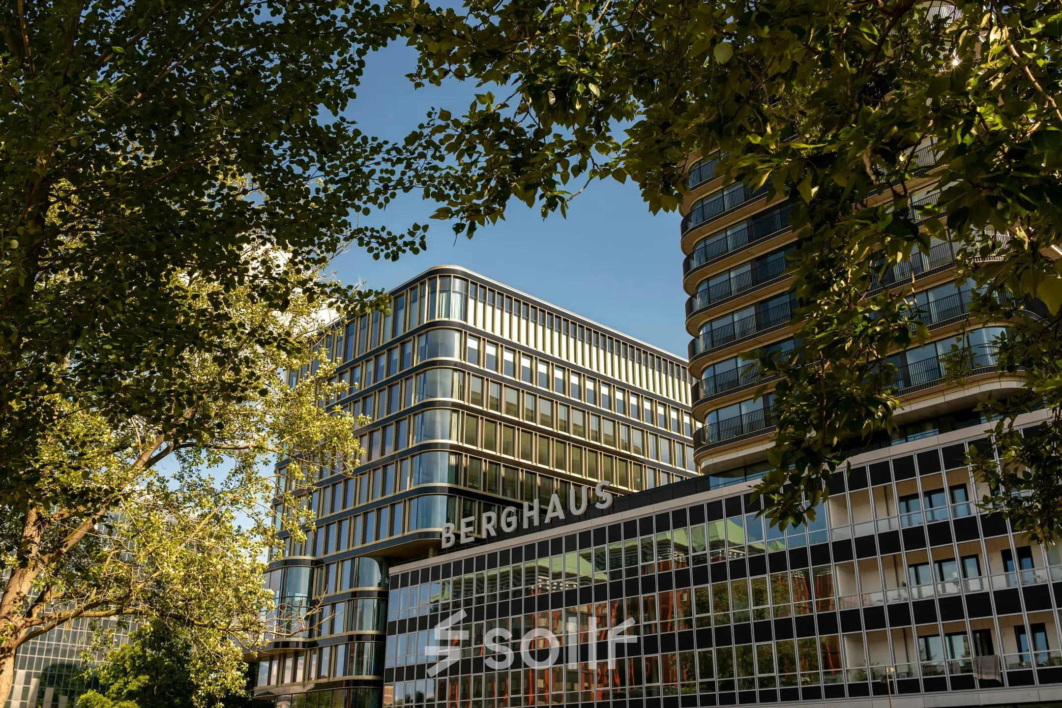 Kantoorpand Berghaus aan het Kon. Wilhelminaplein 4, Amsterdam West, te midden van groene bomen.