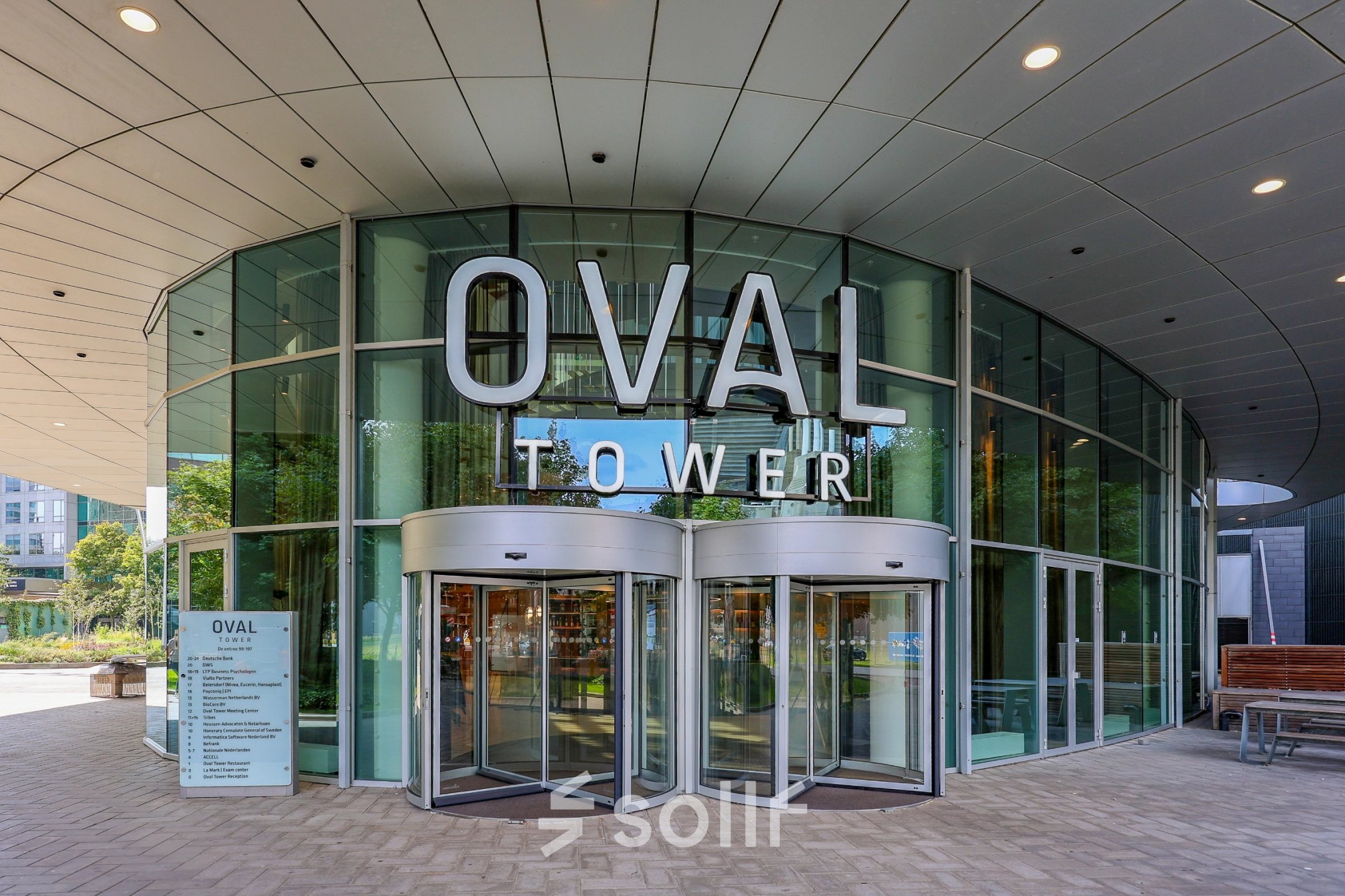 Ingang van een modern kantoorpand aan De Entree 99-197 in Amsterdam Zuid-Oost, met glazen deuren en groot OVAL TOWER bord.