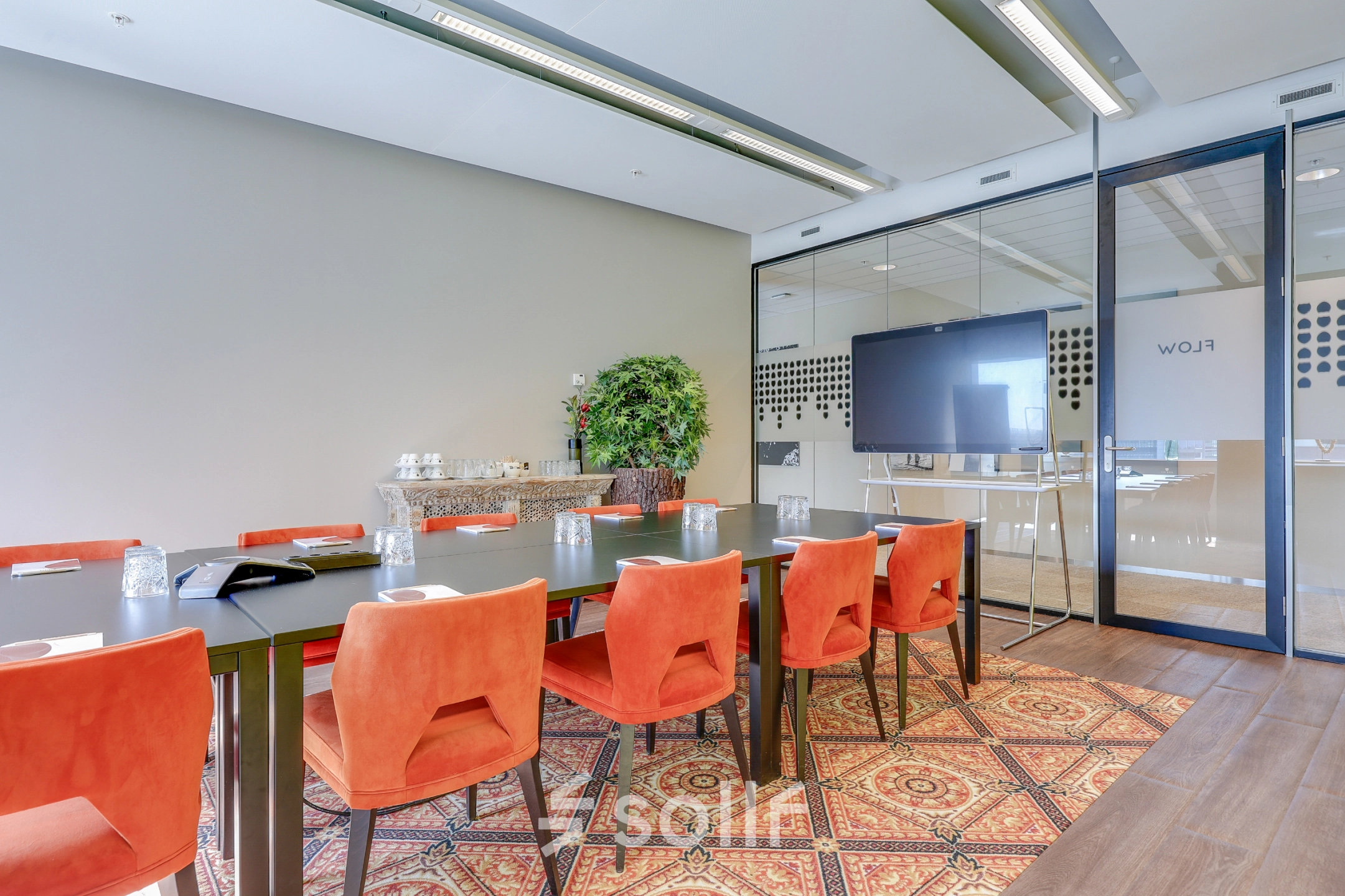Een moderne vergaderruimte in een kantoorpand in Amsterdam Zuid-Oost, met een grote tafel, rode stoelen en een groot scherm. Een ideale plek voor zakelijke bijeenkomsten of kantoorruimte huren.