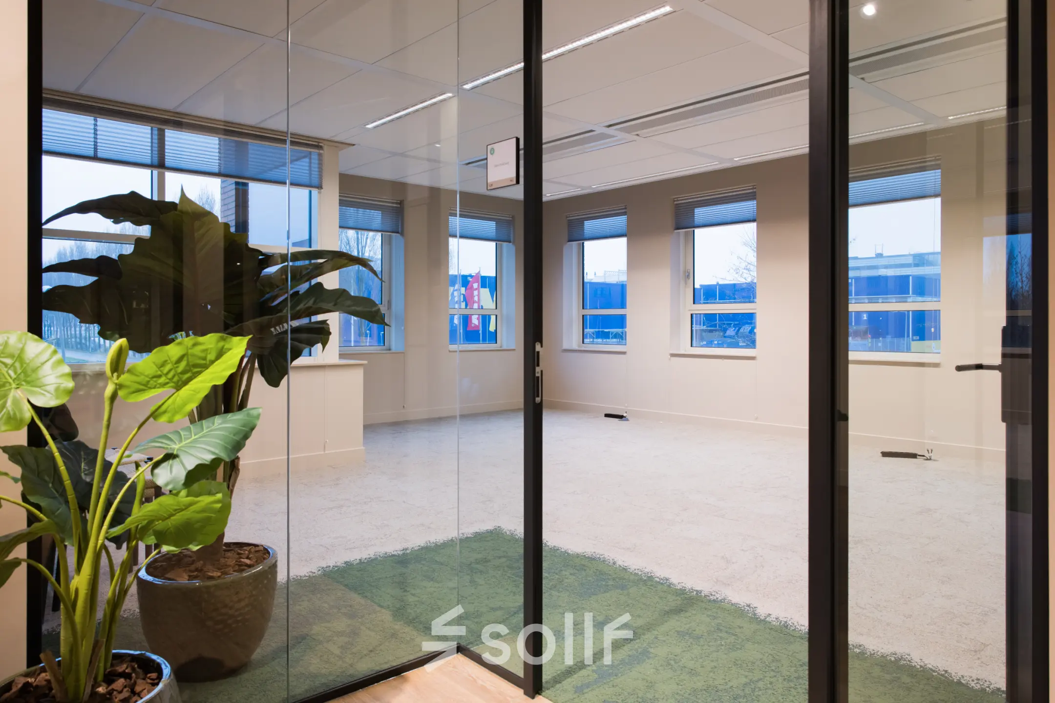 Ongemeubileerd kantoor in Amsterdam Zuid-Oost met moderne glazen deur. Ideaal om kantoorruimte te huren met uitzicht op gebouwen, veel licht en planten voor een frisse uitstraling.