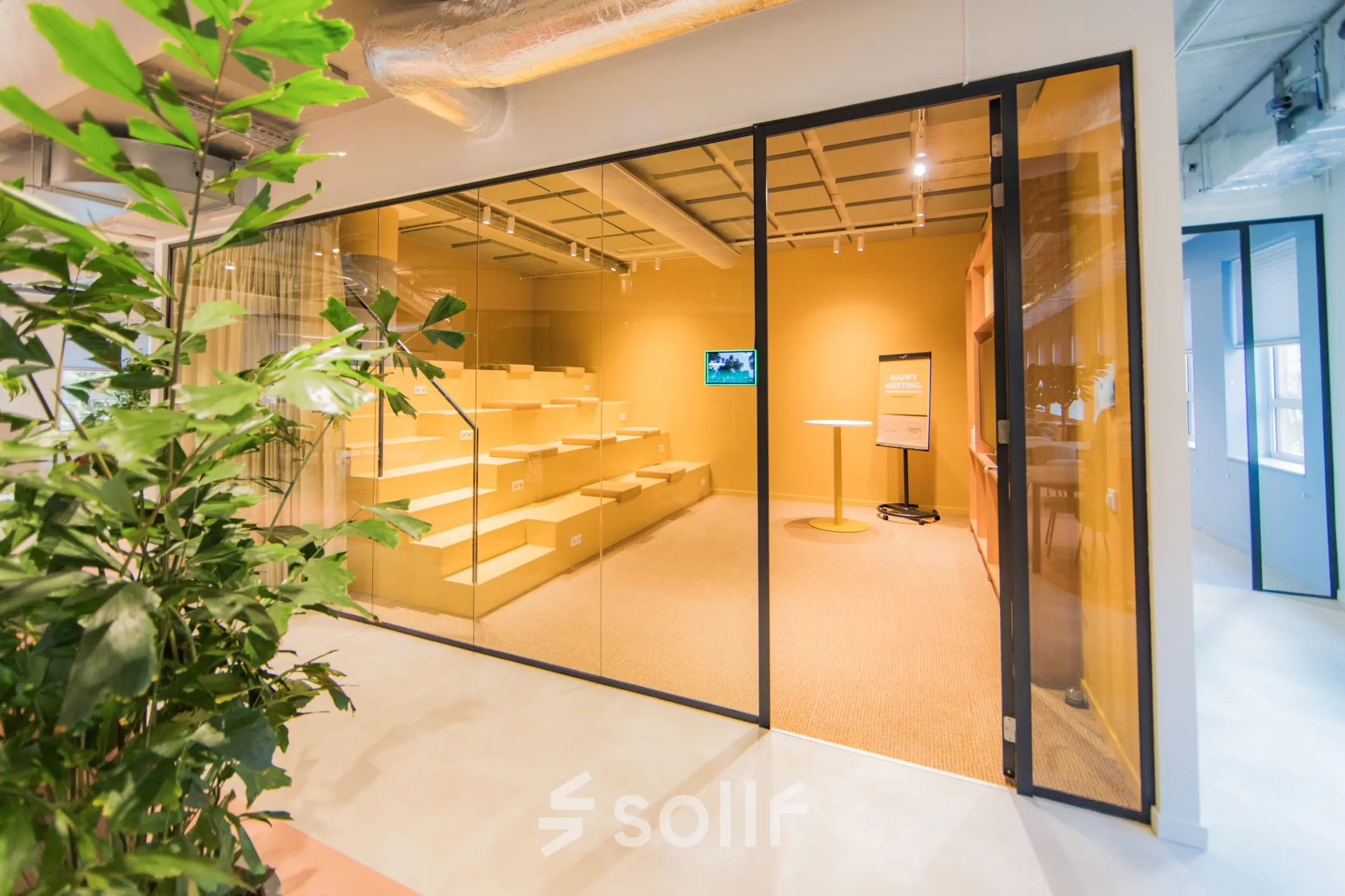 Moderne kantoorlounge met glazen wand, industrieel plafond en zitgedeelte, ideaal voor kantoorruimte huren in Amsterdam Zuid-Oost.