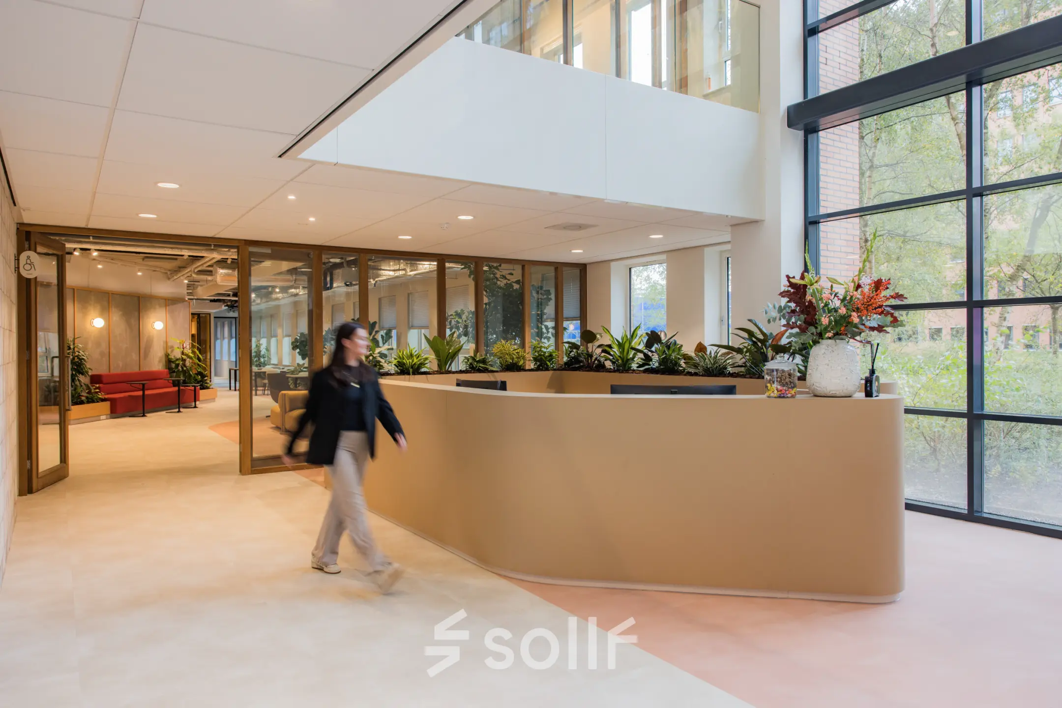 Moderne kantoorpandentree met glazen wanden en een ontvangstbalie, ideaal voor kantoorruimte huren aan Hullenbergweg 109-135 in Amsterdam Zuid-Oost, met een persoon die de receptie passeert.