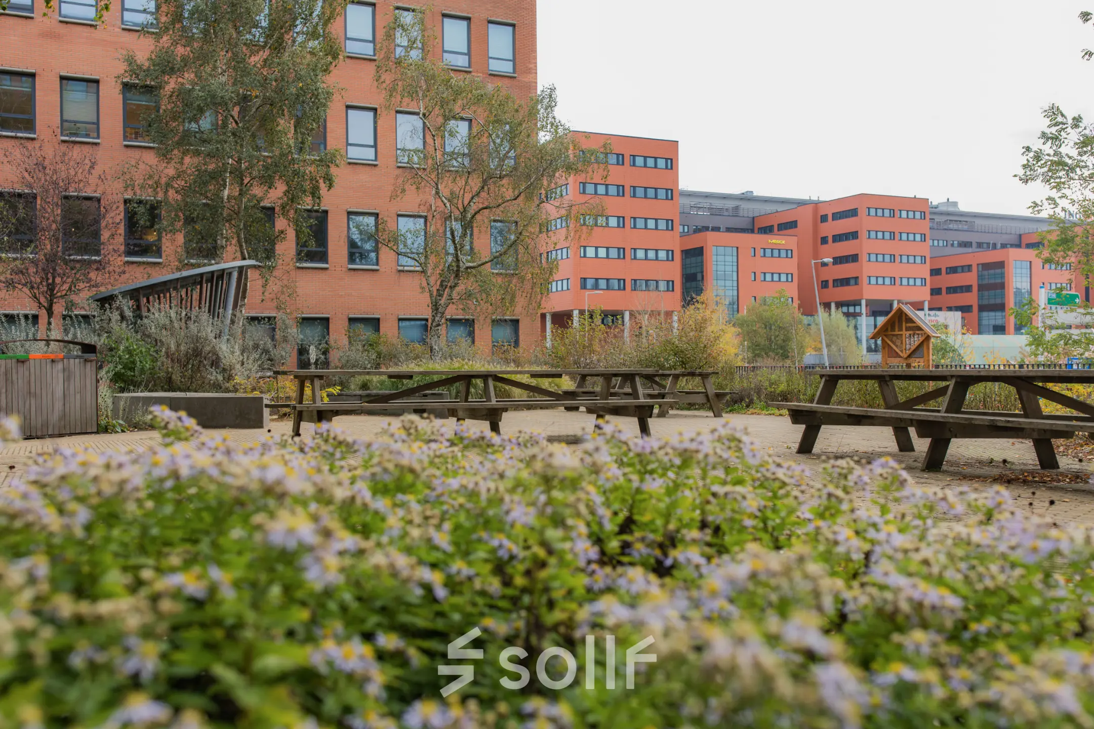 Buitenaanzicht van kantoorpand op Hullenbergweg 109-135 in Amsterdam Zuid-Oost met groene omgeving en picknickbanken, ideaal voor huur.