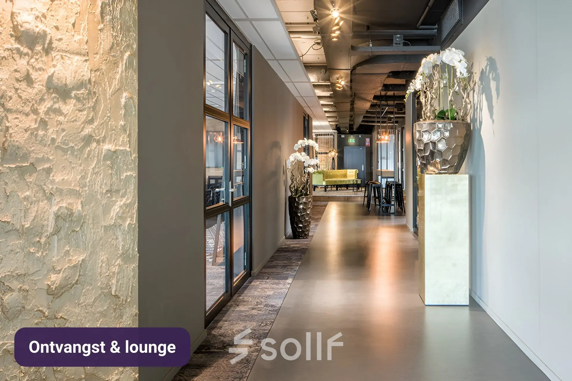 Verlichte gang van een kantoorpand op Johan Cruijff Boulevard 89, Amsterdam Zuid-Oost, met moderne inrichting, loungebanken en planten. Ideaal voor kantoorruimte huren vanwege veelzijdigheid.
