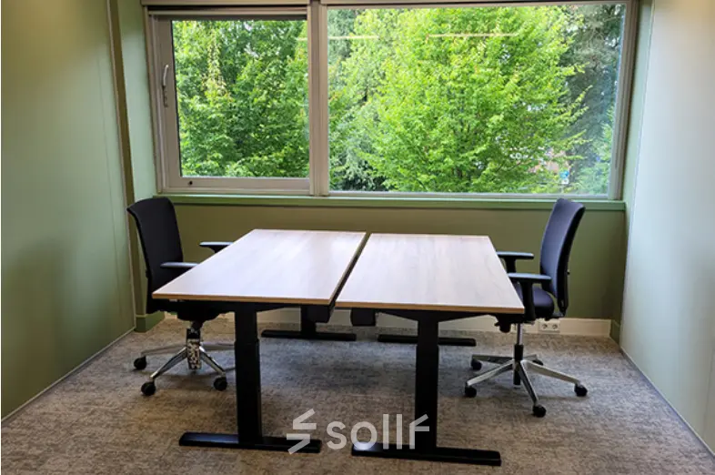 Kantoorruimte huren op Johan Cruijff Boulevard 89 in Amsterdam Zuid-Oost met twee bureaus en stoelen voor een groene muur met grote ramen.