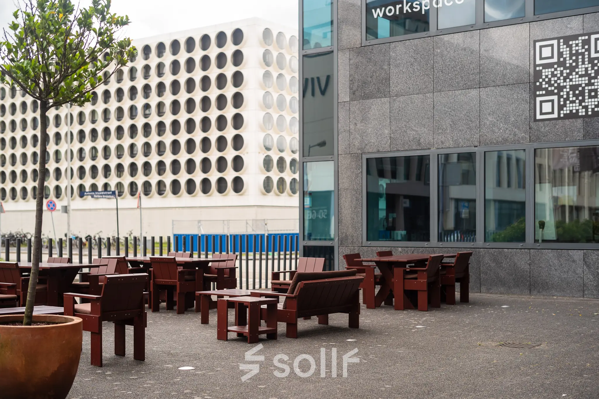 Exterieur van een kantoorpand aan de Barbara Strozzilaan 101, Amsterdam Zuidas, met houten zitplaatsen buiten. Ideaal voor wie kantoorruimte huren wil in een dynamisch omgeving.