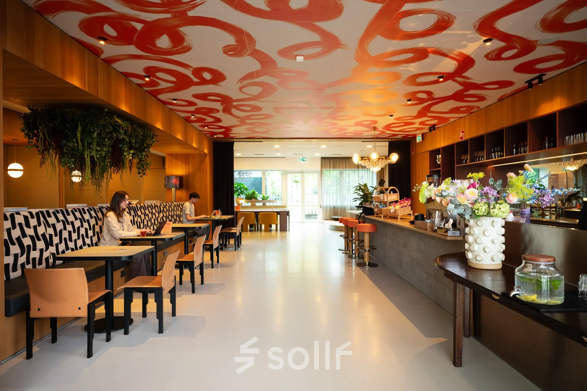 Moderne kantoorruimte op Barbara Strozzilaan 101, Amsterdam Zuidas, met kleurrijk interieur, stijlvolle zitplaatsen en een bar. Twee mensen werken op laptops in een ontspannen setting.