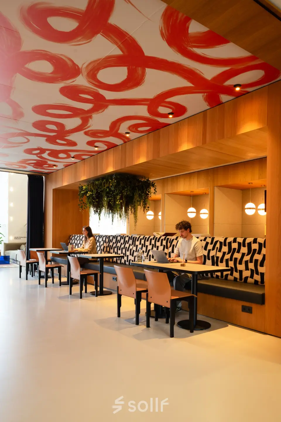 Stijlvolle kantoorruimte op Barbara Strozzilaan 101, Amsterdam Zuidas, met moderne houten afwerking, kleurrijke plafondkunst en comfortabele zitgelegenheden. Personen zijn bezig met laptops. Geschikt voor kantoorruimte huren.