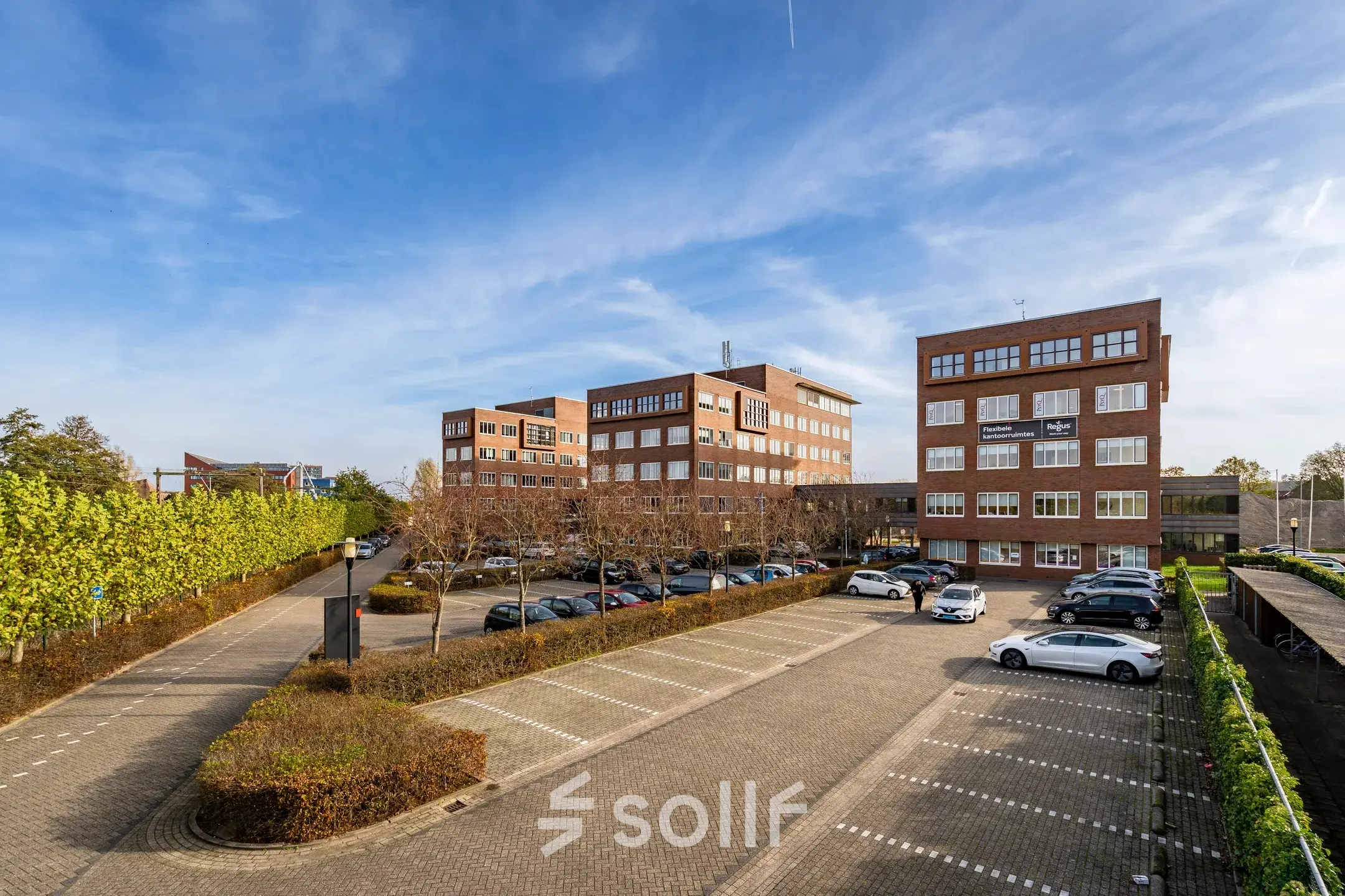 Exterieur van het kantoorpand op Het Rietveld 55-59 in Apeldoorn, omgeven door parkeerruimte en groene begroeiing.