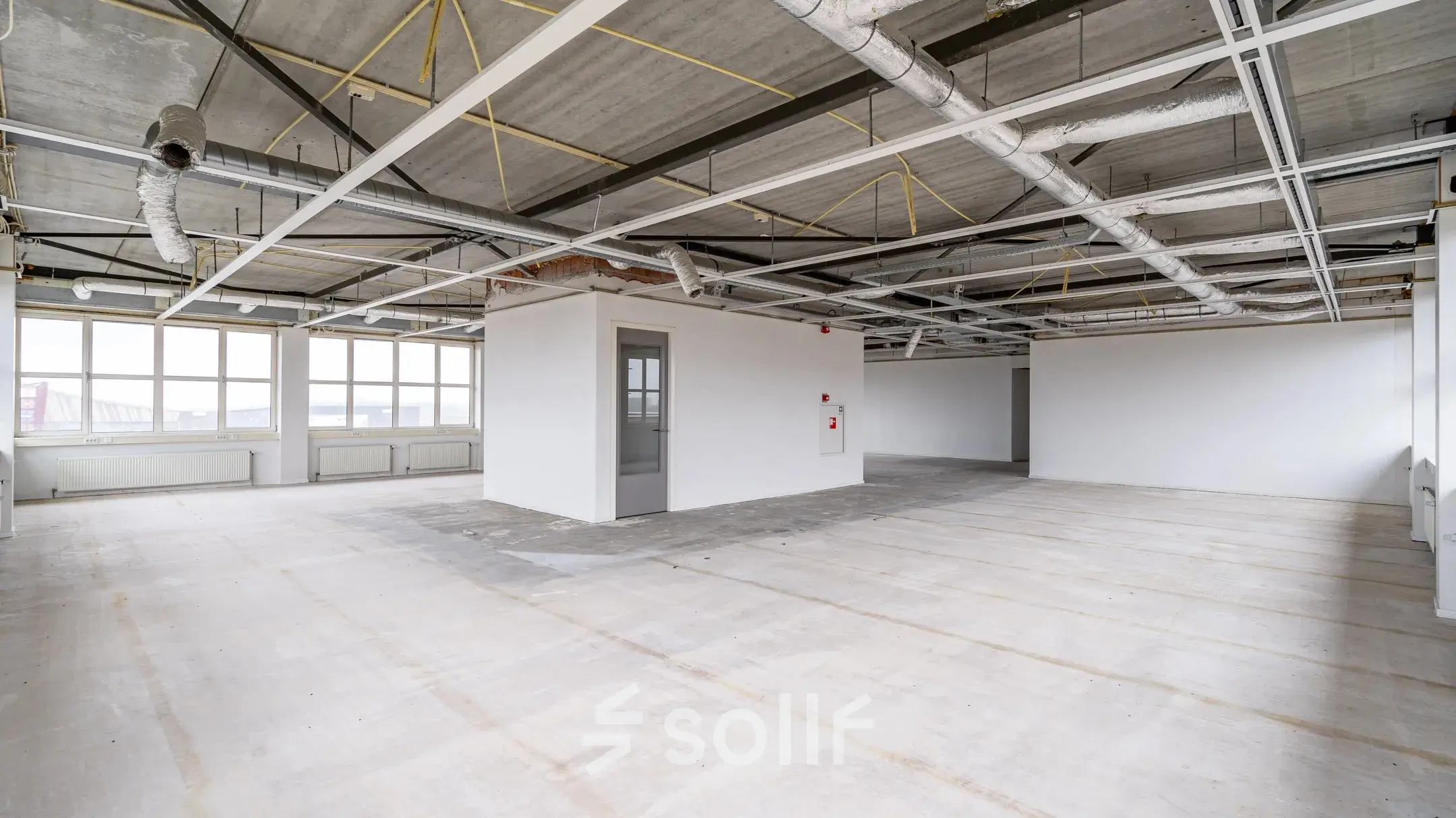 Ongemeubileerde kantoorruimte te huur in Apeldoorn met industriële plafonds en grote ramen voor veel natuurlijk licht.