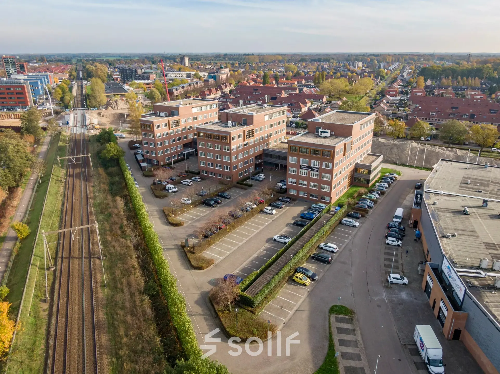 Luchtfoto van het kantoorpand aan Het Rietveld 55-59 in Apeldoorn, omgeven door parkeerplaatsen en nabij het spoor. Ideaal voor wie een kantoorruimte wil huren.