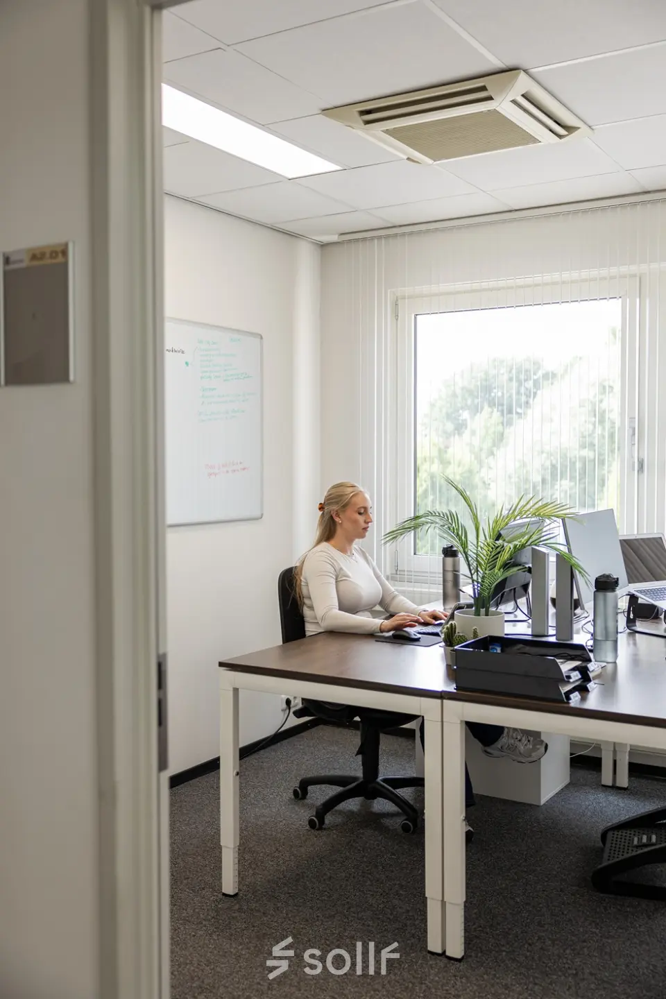 Een licht kantoor op Vlamoven 34 in Arnhem IJsseloord met een bureau, computer en een plant. Een persoon voert werk uit aan het bureau. Ideale ruimte voor kantoorruimte huren.