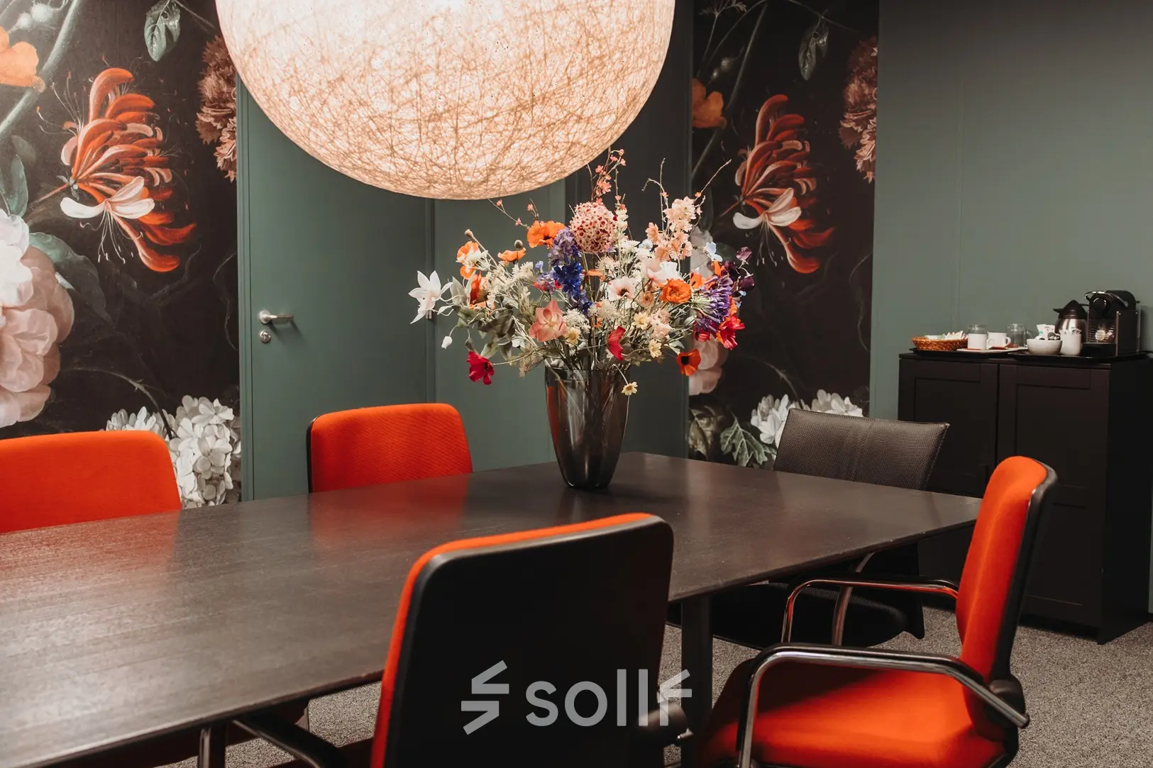 Stijlvolle kantoorruimte huren in Arnhem IJsseloord aan Vlamoven 34 met moderne vergadertafel, felgekleurde stoelen en decoratieve bloemenvaas.