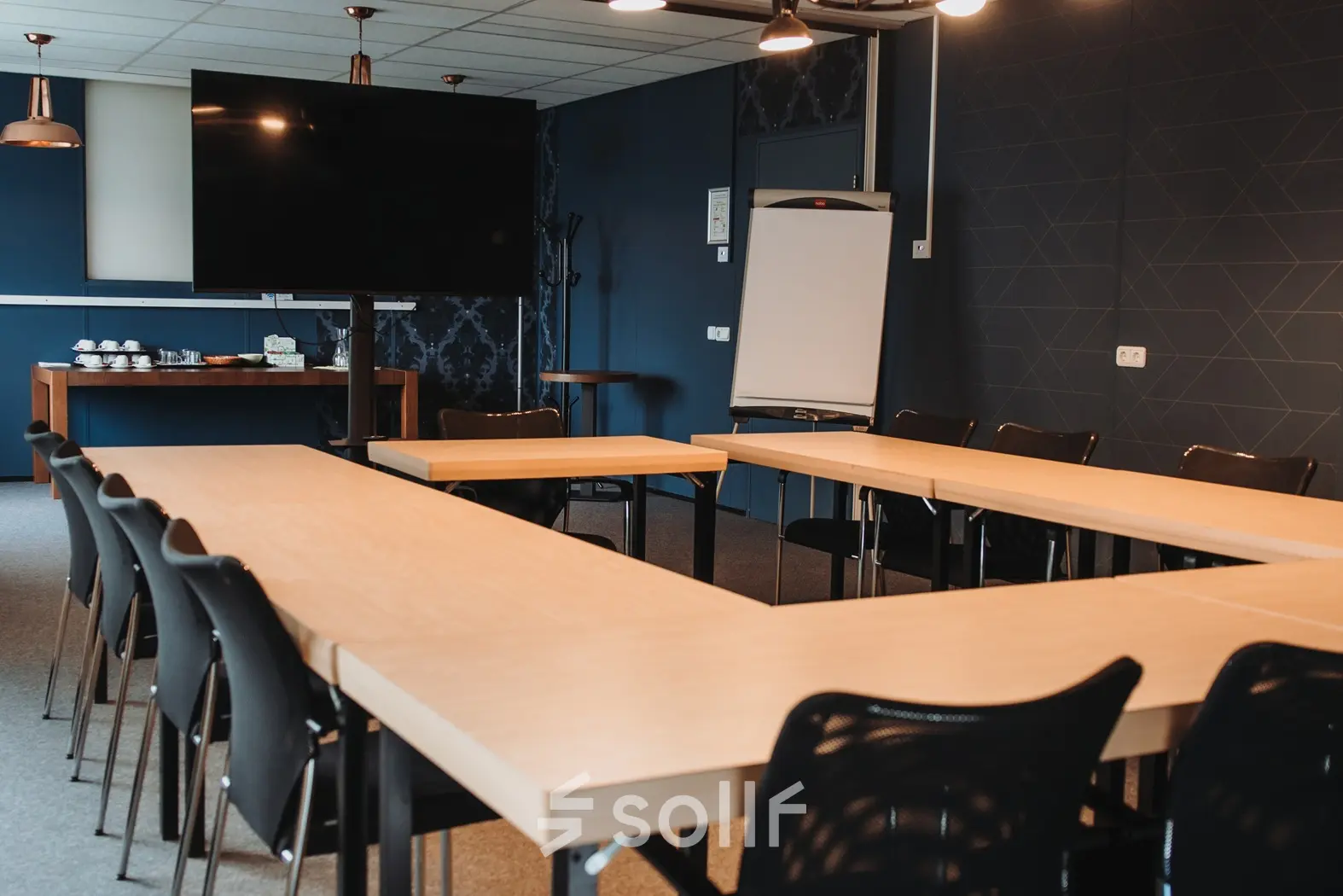 Vergaderruimte in Arnhem IJsseloord met een U-vormige opstelling van houten tafels, zwarte stoelen en een groot scherm. Kantoorruimte huren in kantoorpand op Vlamoven 34, uitgerust voor zakelijke bijeenkomsten.