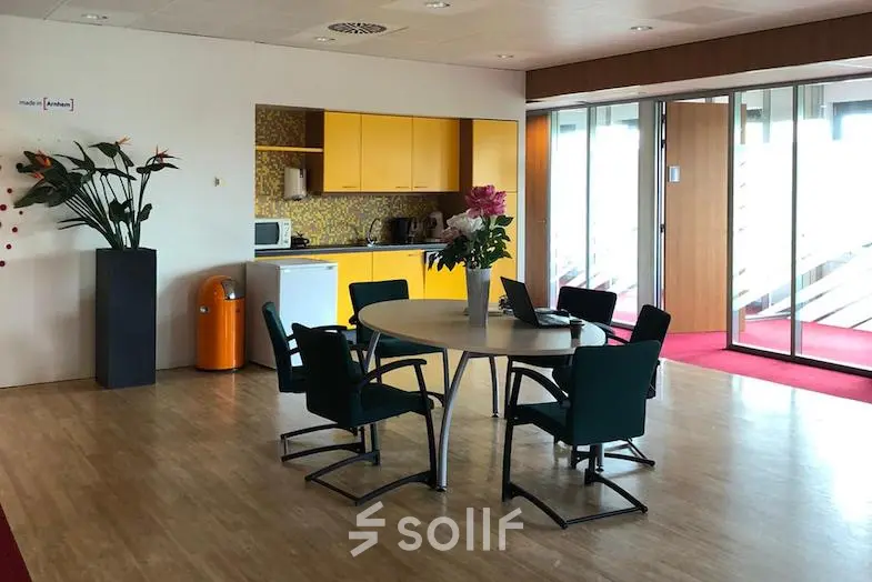 Foto van een gemeubileerd kantoor in Arnhem-Zuid met ronde tafel en stoelen, ideaal voor een kort overleg. Geel keukentje op de achtergrond. Kantoorruimte huren biedt praktische werkplekken.