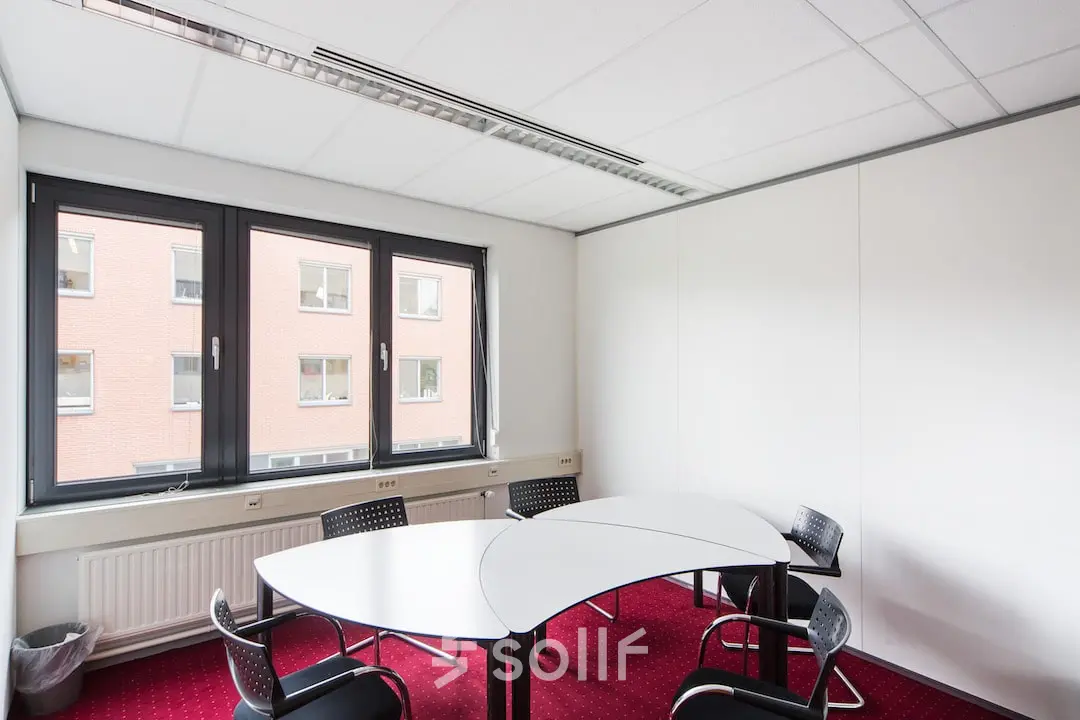 Kantoorruimte huren in Arnhem Zuid aan de Kronenburgsingel 525. Gelegen in een ruim, goed verlicht kantoor met rode vloerbedekking en moderne stoelen rondom een vergadertafel. Ideaal voor zakelijke bijeenkomsten.