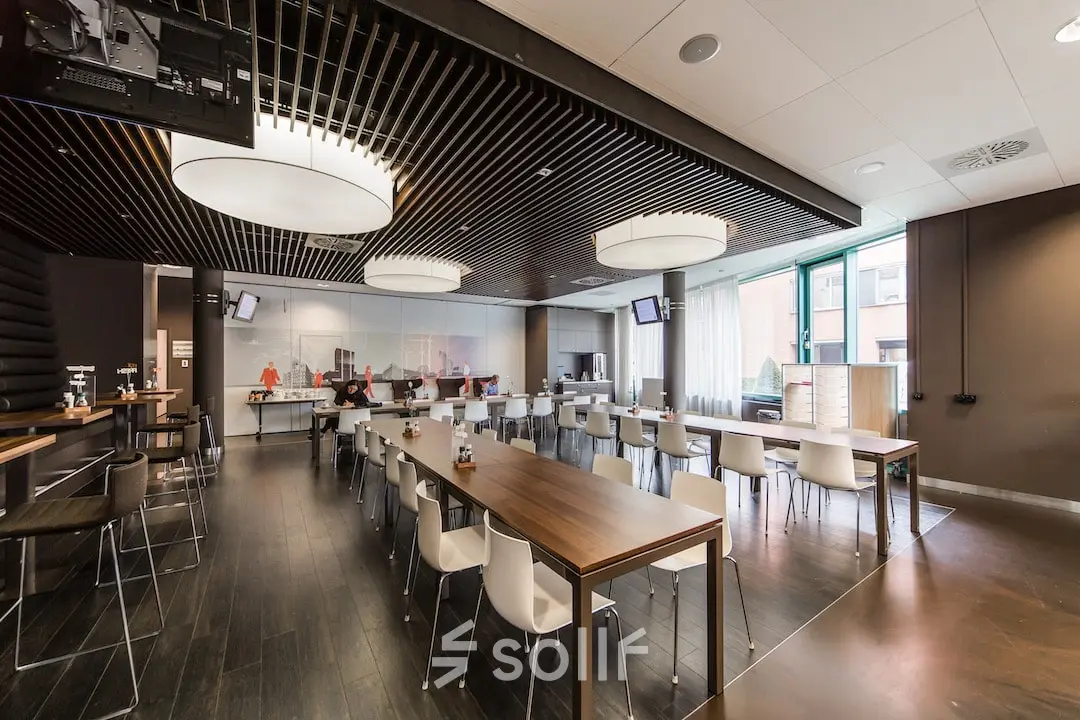 Moderne kantoorruimte in Arnhem Zuid met ruime tafels en stijlvolle verlichting, bij Kronenburgsingel 525. Mensen zijn druk aan het werk in een open en lichte omgeving.