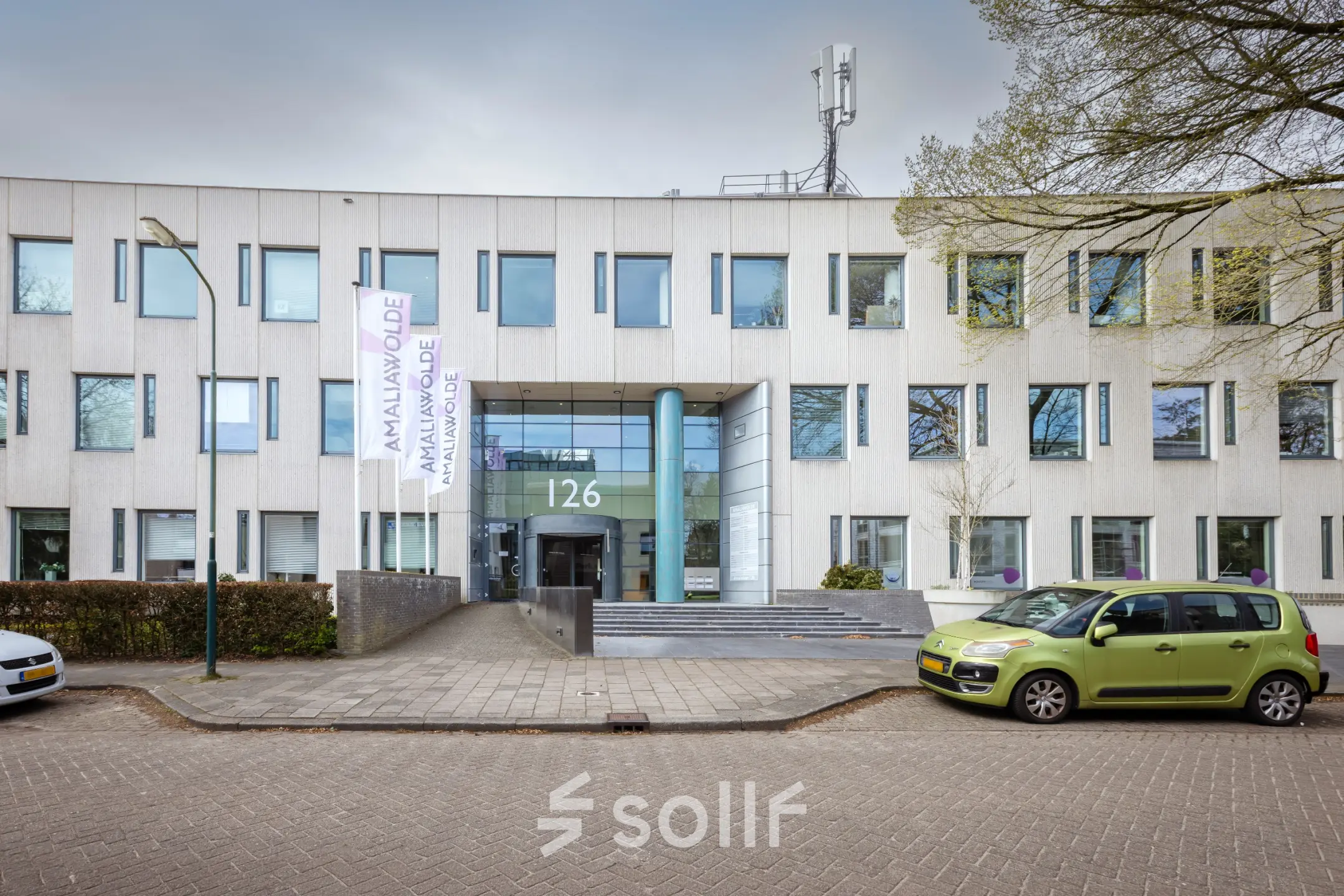Vooraanzicht van kantoorpand op Amalialaan 126 in Baarn; modern gebouw met strakke gevel en parkeerplaats. Ideaal voor kantoorruimte huren.
