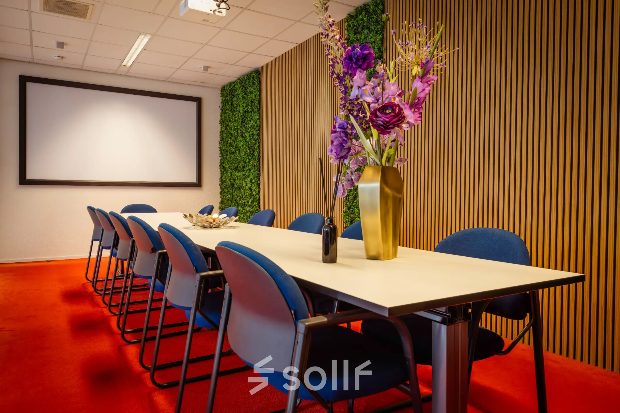 Vergaderruimte in kantoorpand op Amalialaan 126, Baarn met moderne tafel, blauwe stoelen en decoratieve bloemen. Ideaal voor kantoorruimte huren.