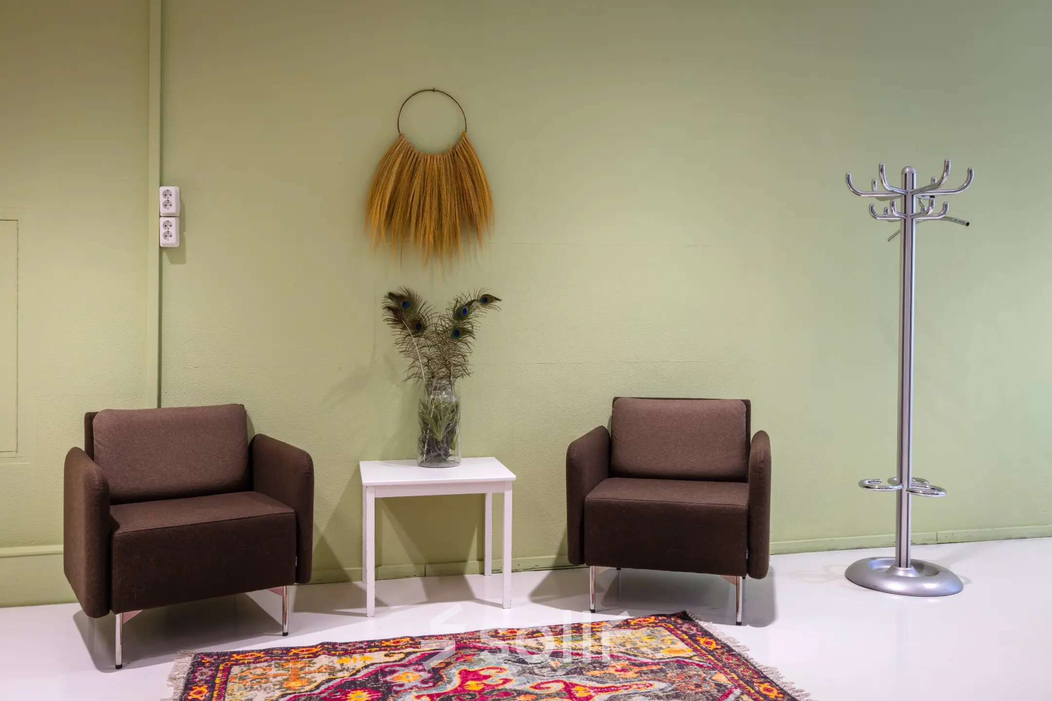 Kantoor op de Amalialaan 126 in Baarn met twee stoelen, een bijzettafel en kleerhanger in kleurrijke ruimte. Optie voor kantoorruimte huren in modern kantoorpand.