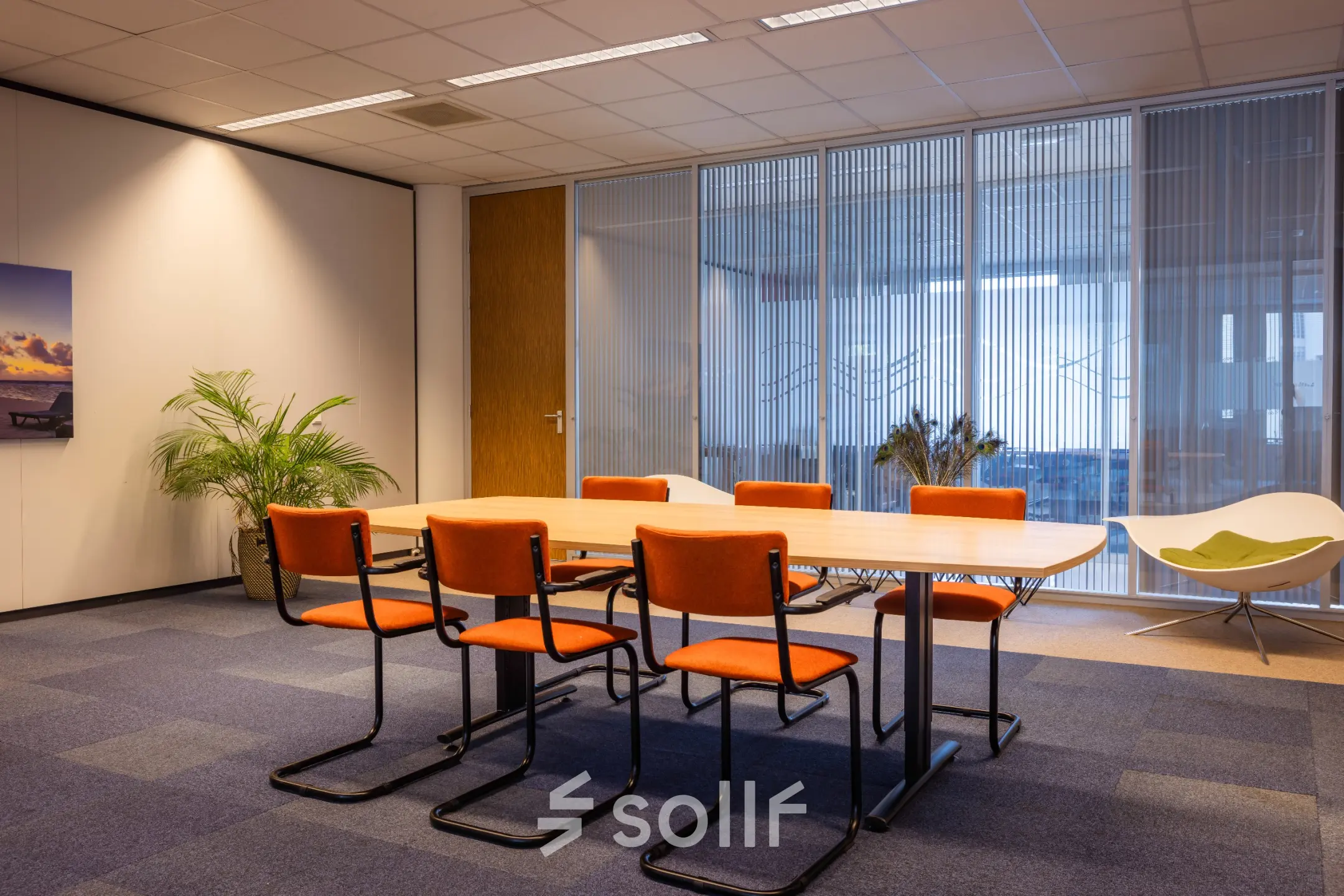 Kantoorruimte huren op Amalialaan 126 in Baarn met een vergadertafel en oranje stoelen, omringd door rustige decoraties en een glazen wand.