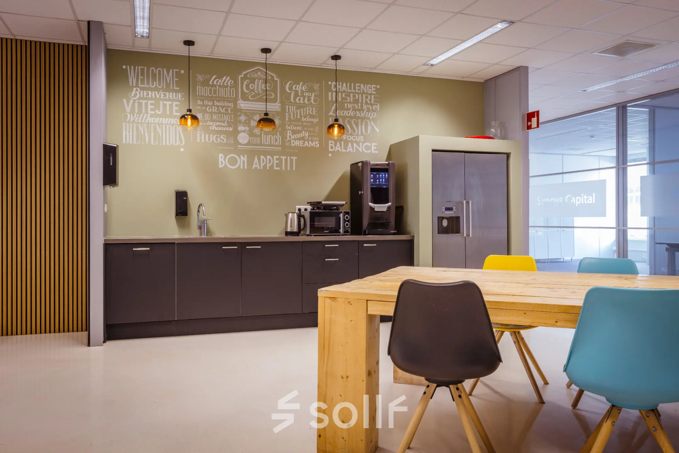 Moderne pantry in kantoorpand met een houten tafel, kleurrijke stoelen en keukenapparatuur op Amalialaan 126, Baarn.