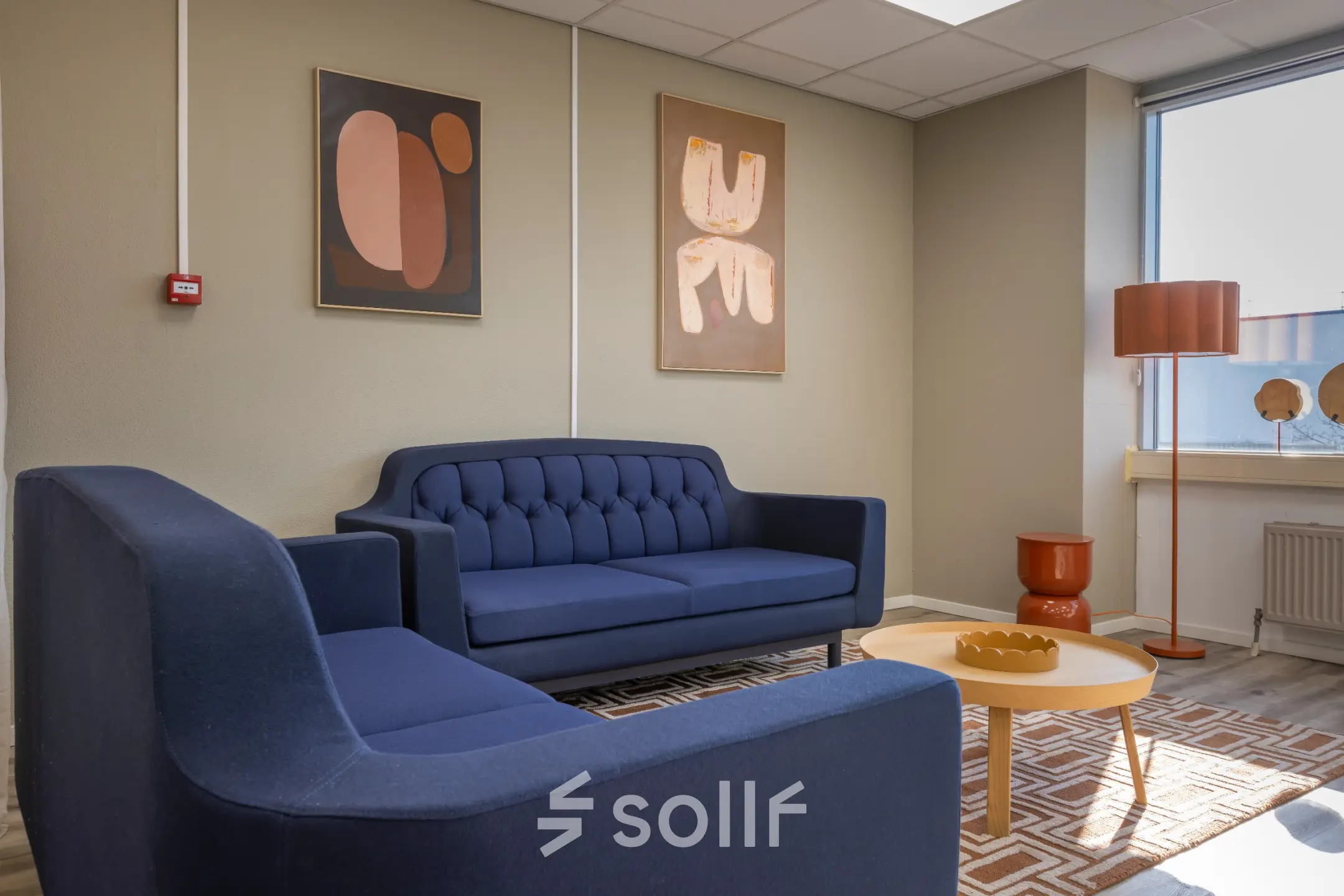 Stijlvolle lounge in kantoorpand aan de Kamerlingh Onnesweg 10, Barendrecht, met donkerblauwe banken, kunst aan de muur en houten salontafel. Kantoorruimte huren in een uitnodigende omgeving.