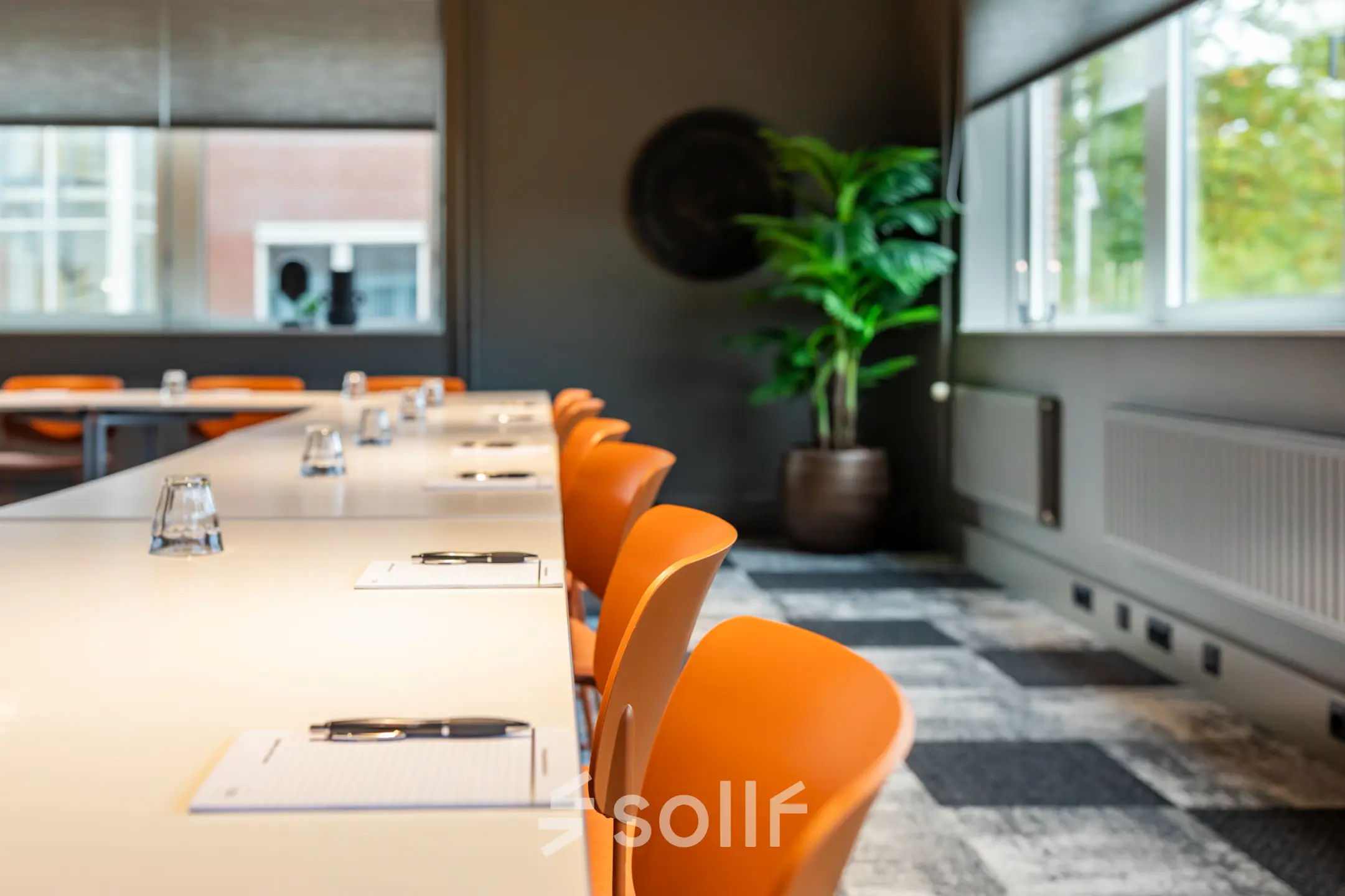 Moderne kantoorruimte met feloranje stoelen en een lange tafel, klaar voor bespreking of vergadering. Ideaal voor wie een kantoorpand wil huren in Barneveld.