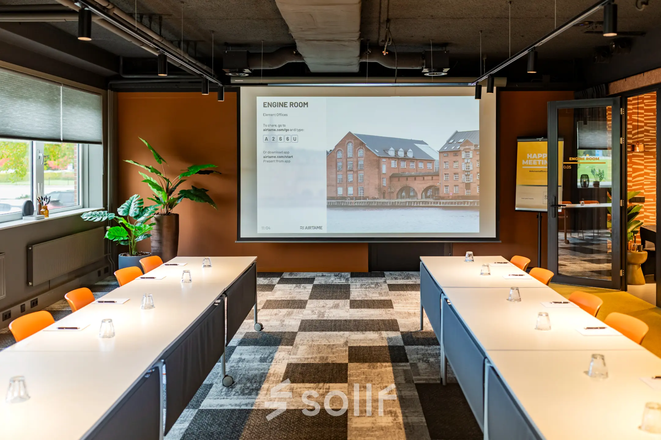 Vergaderruimte in Barneveld met meerdere tafels, stoelen en een groot scherm, ideaal voor kantoorruimte huren. Modern kantoorpand aan Baron van Nagellstraat 136, ruim en functioneel in gebruik.