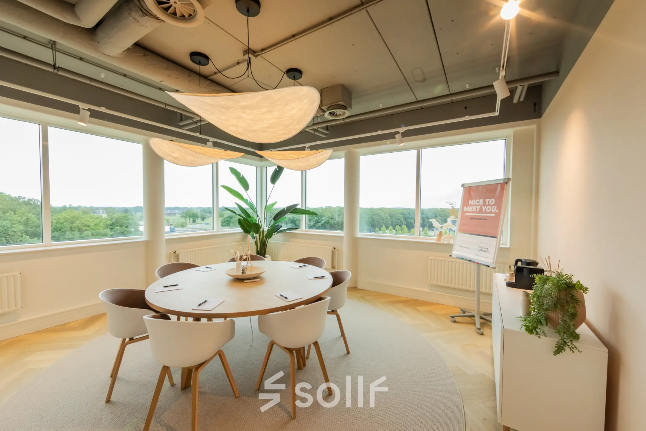 Moderne, lichte kantoorruimte met ronde tafel en stoelen, geschikt voor vergaderingen. De grote ramen bieden uitzicht op groen landschap. Perfect om een kantoorruimte te huren in Barneveld.